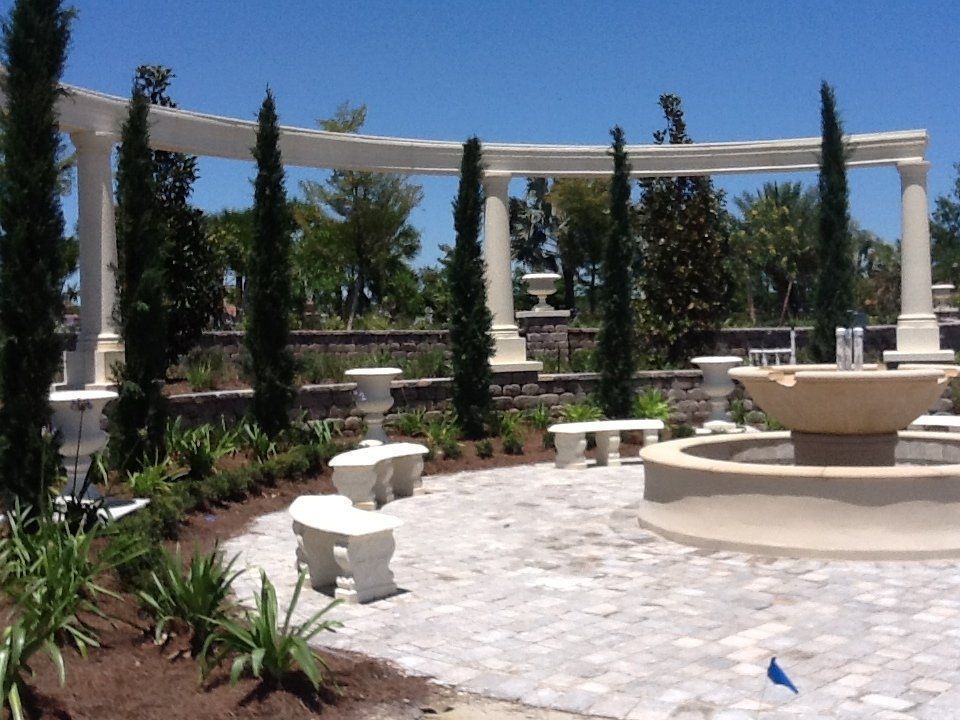 Sunny courtyard with white stone benches, a fountain, and tall columns under a blue sky
