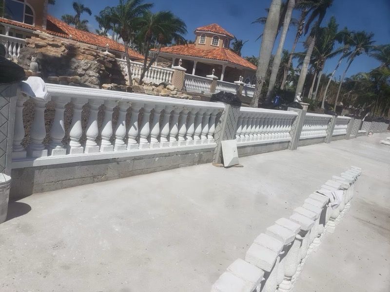 White balustrade along a sunny walkway with palm trees and a tiled-roof building in the background