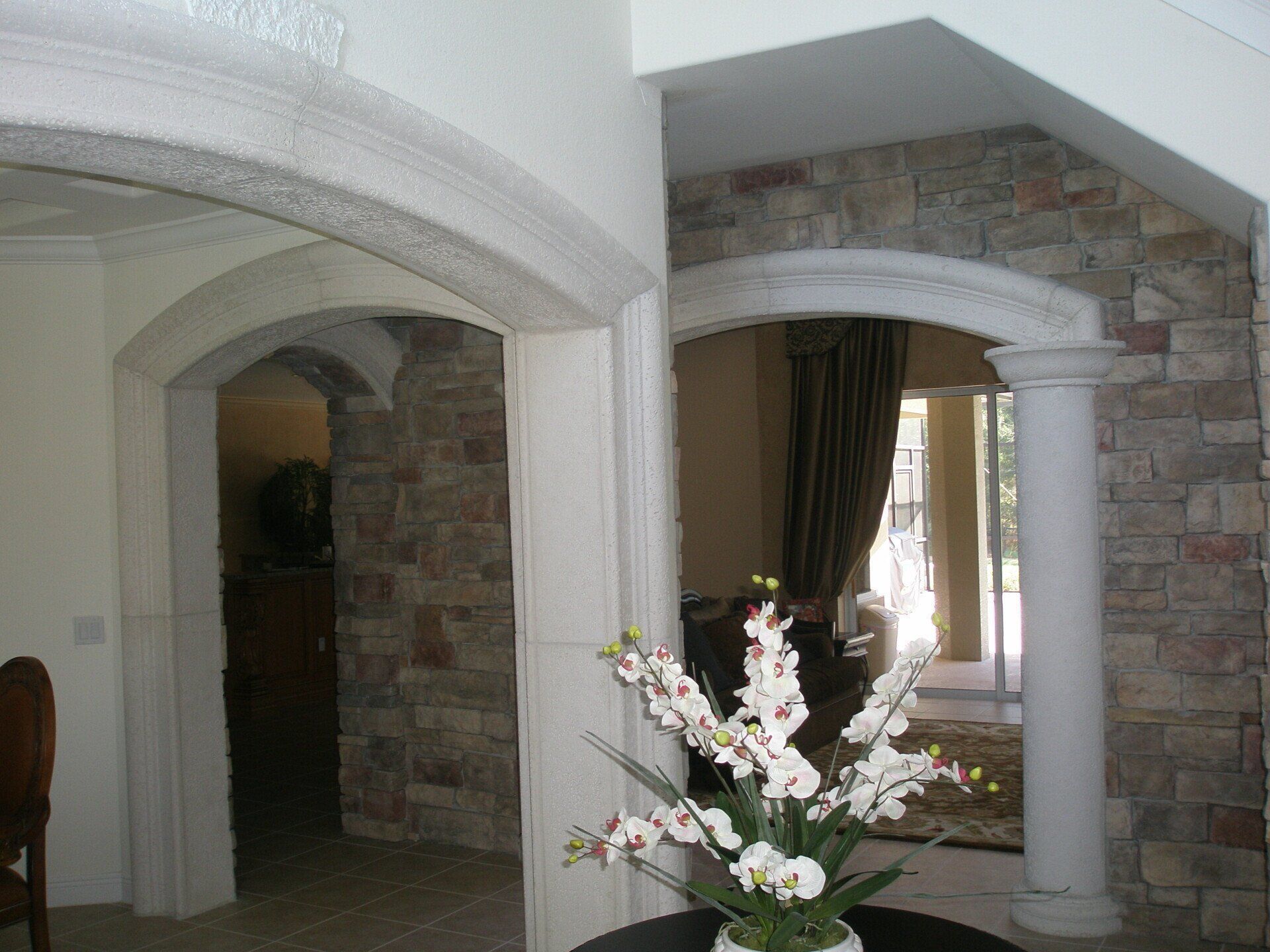 Living room with arched doorways, stone accent walls, and a white flower arrangement in the foreground