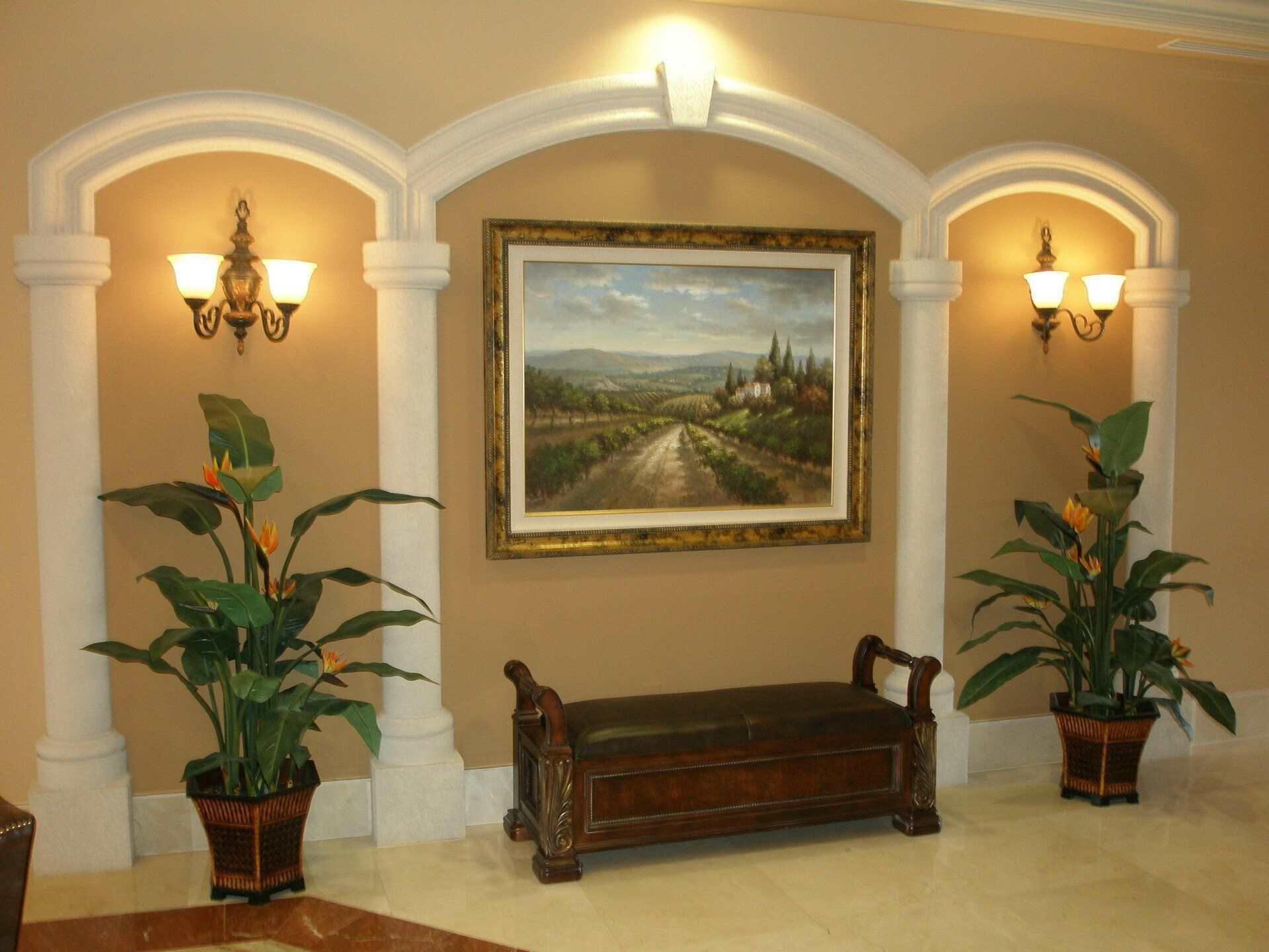 Elegant lobby with framed landscape painting, bench, wall sconces, and potted plants in warm neutral tones