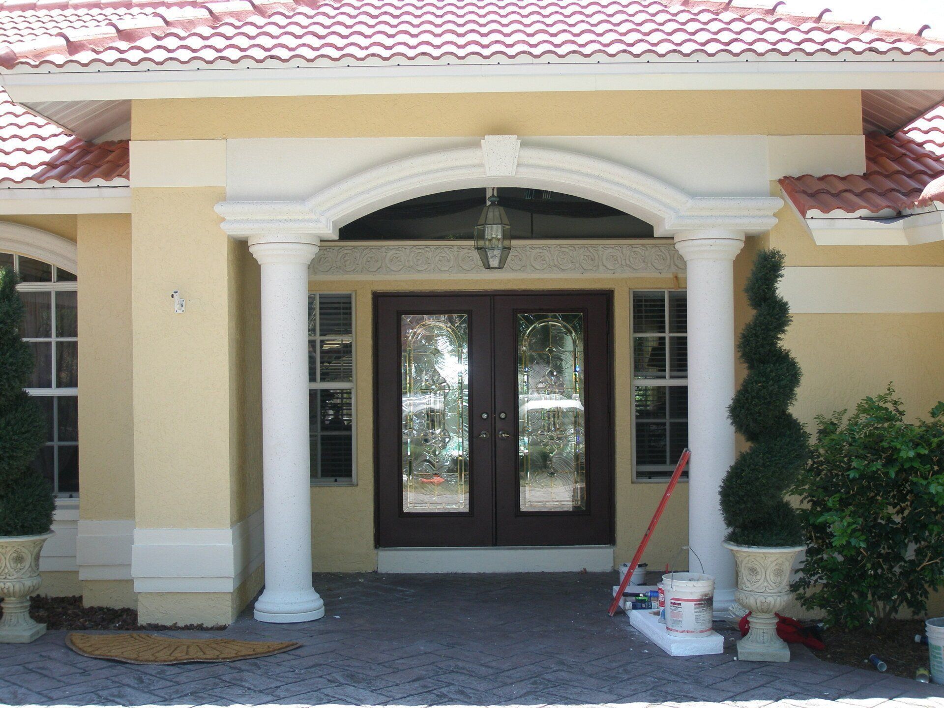 Front entrance of a house with white columns, double glass doors, and potted plants by the doorway