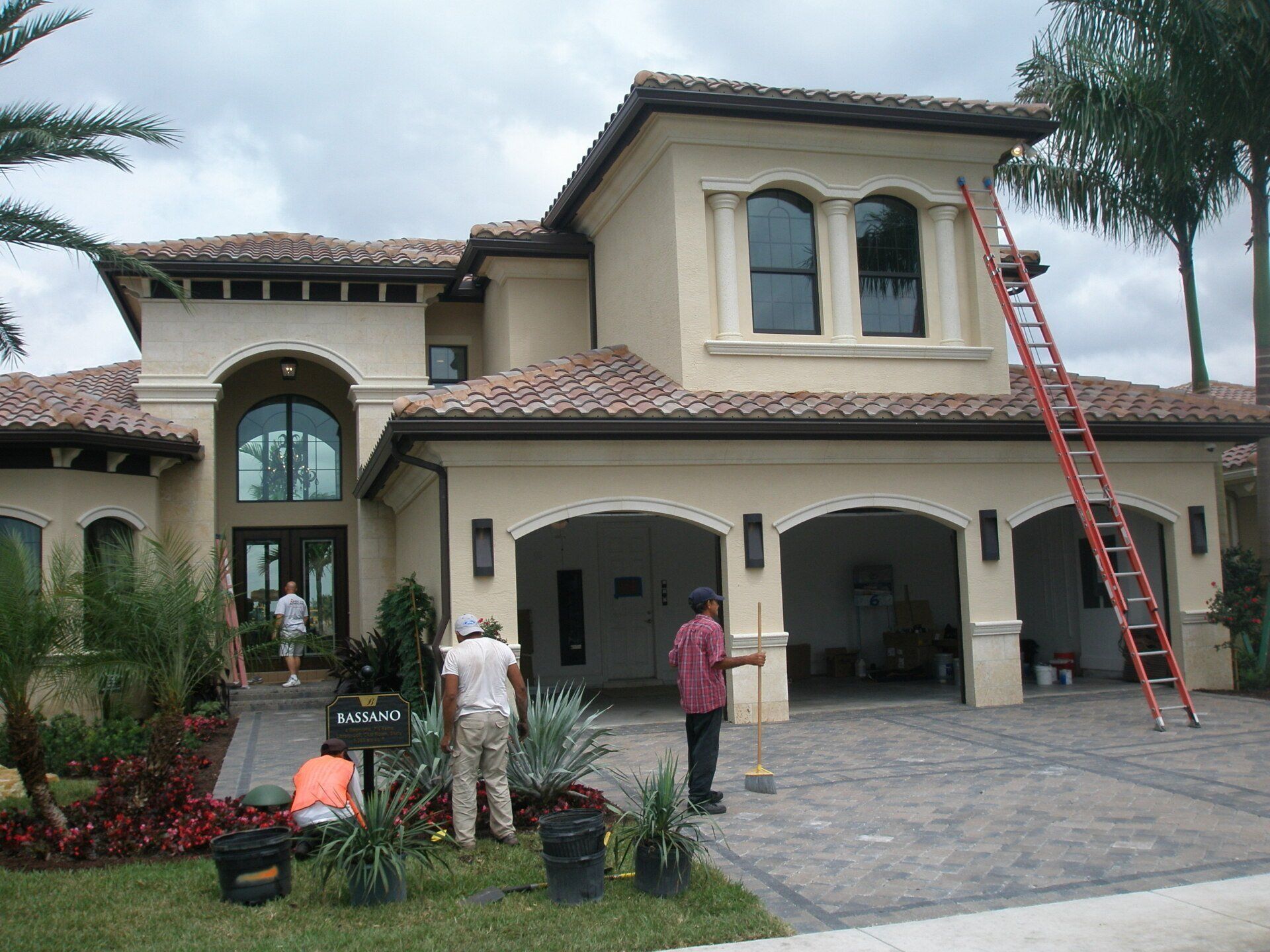 Workers on a ladder painting the front of a large stucco house with tiled roof.