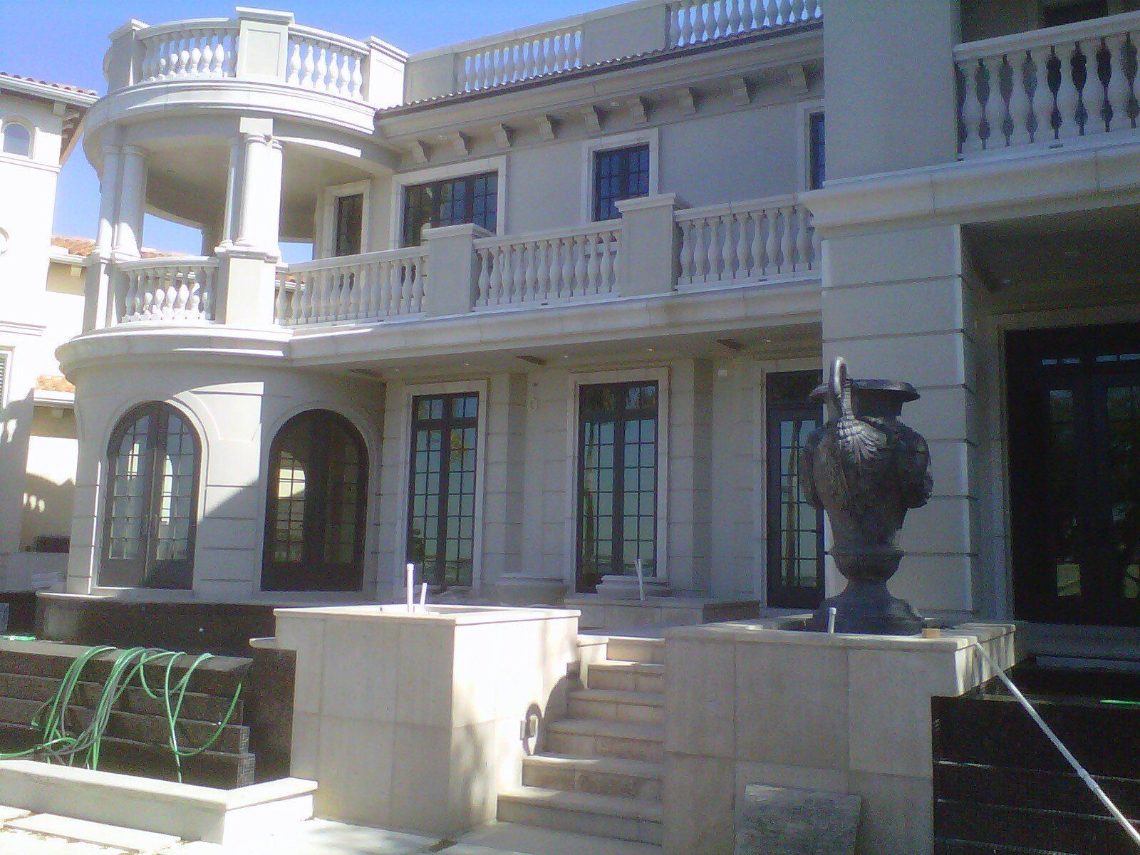 Grand mansion facade with balconies, arched windows, stairs, and a large urn statue by the entrance