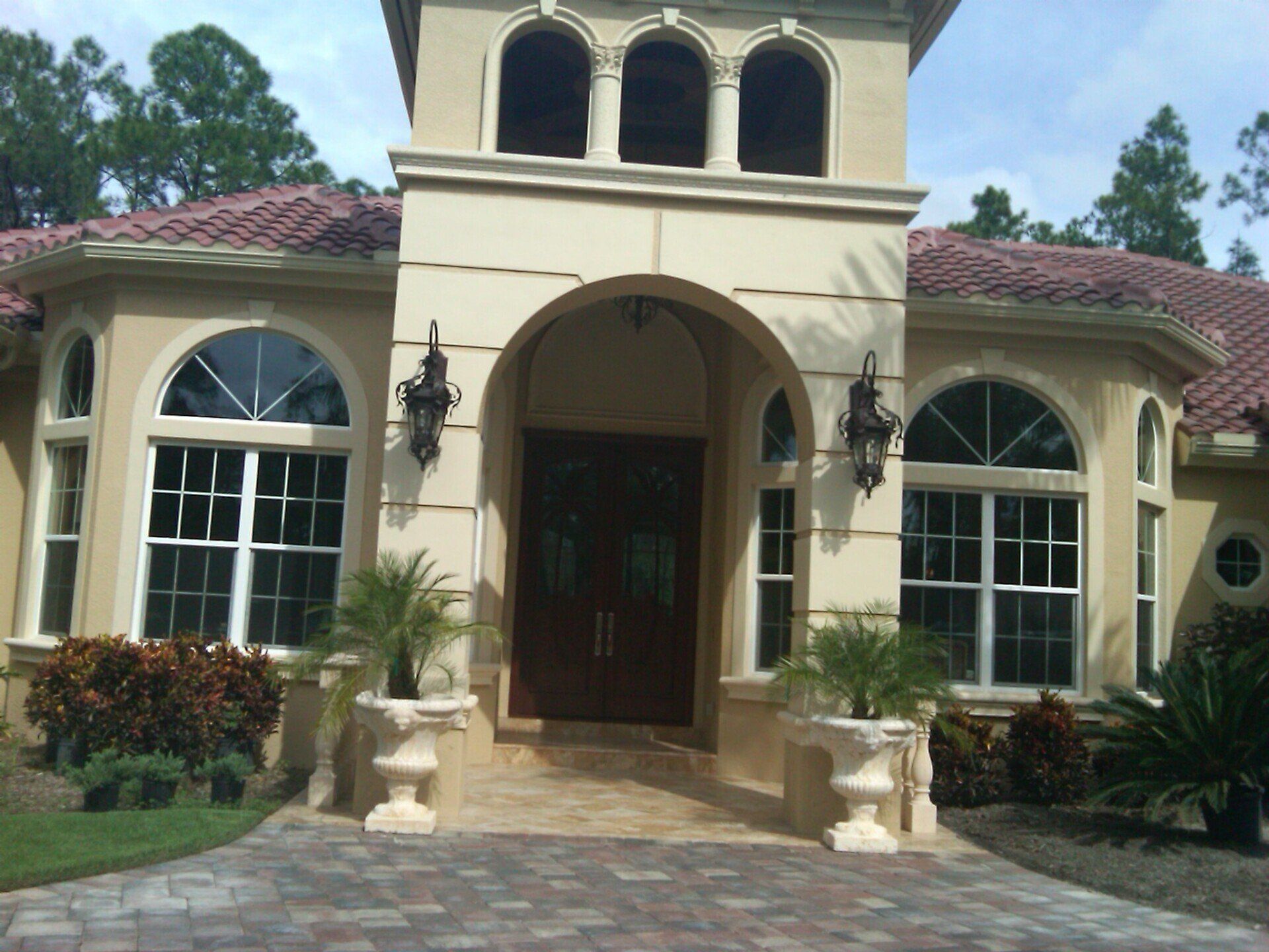 Front view of a cream-colored Mediterranean-style house with arched entry, red-tiled roof, and manicured landscaping