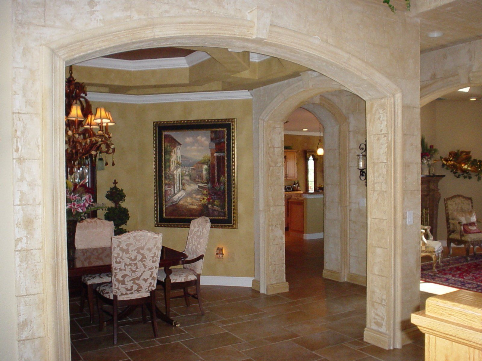 Elegant dining room with arched doorways, chandelier, and framed artwork on beige stone walls