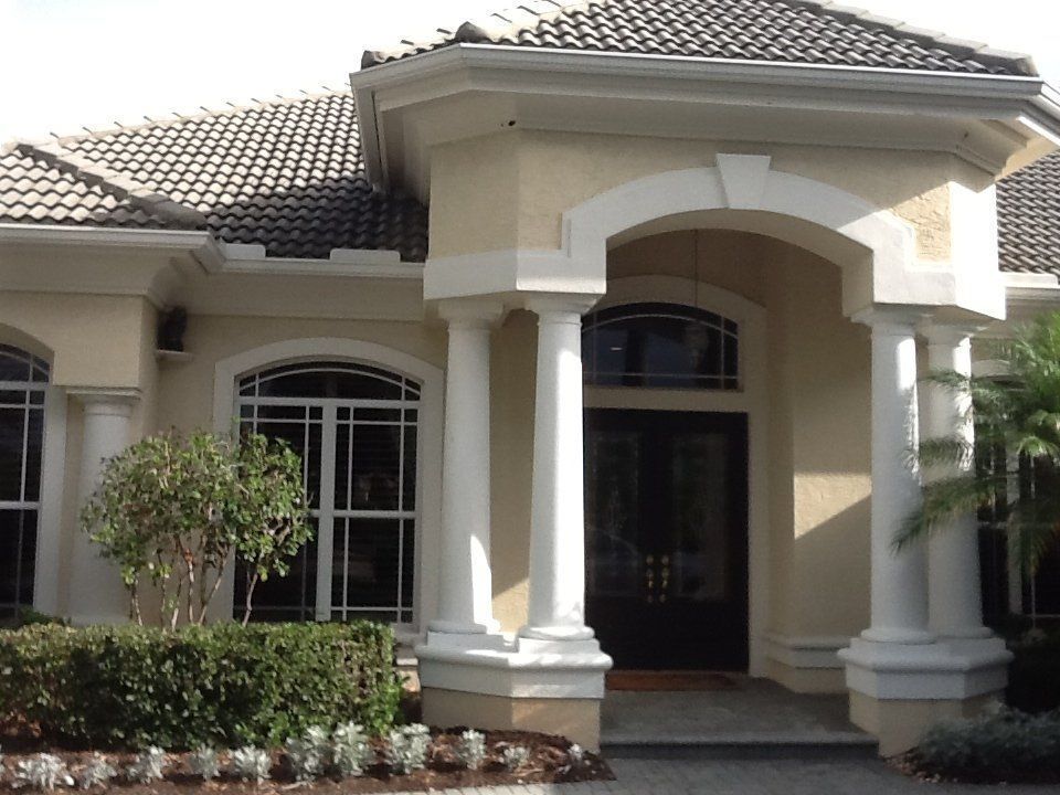 Front entrance of a beige stucco house with arched columns and a tiled roof.