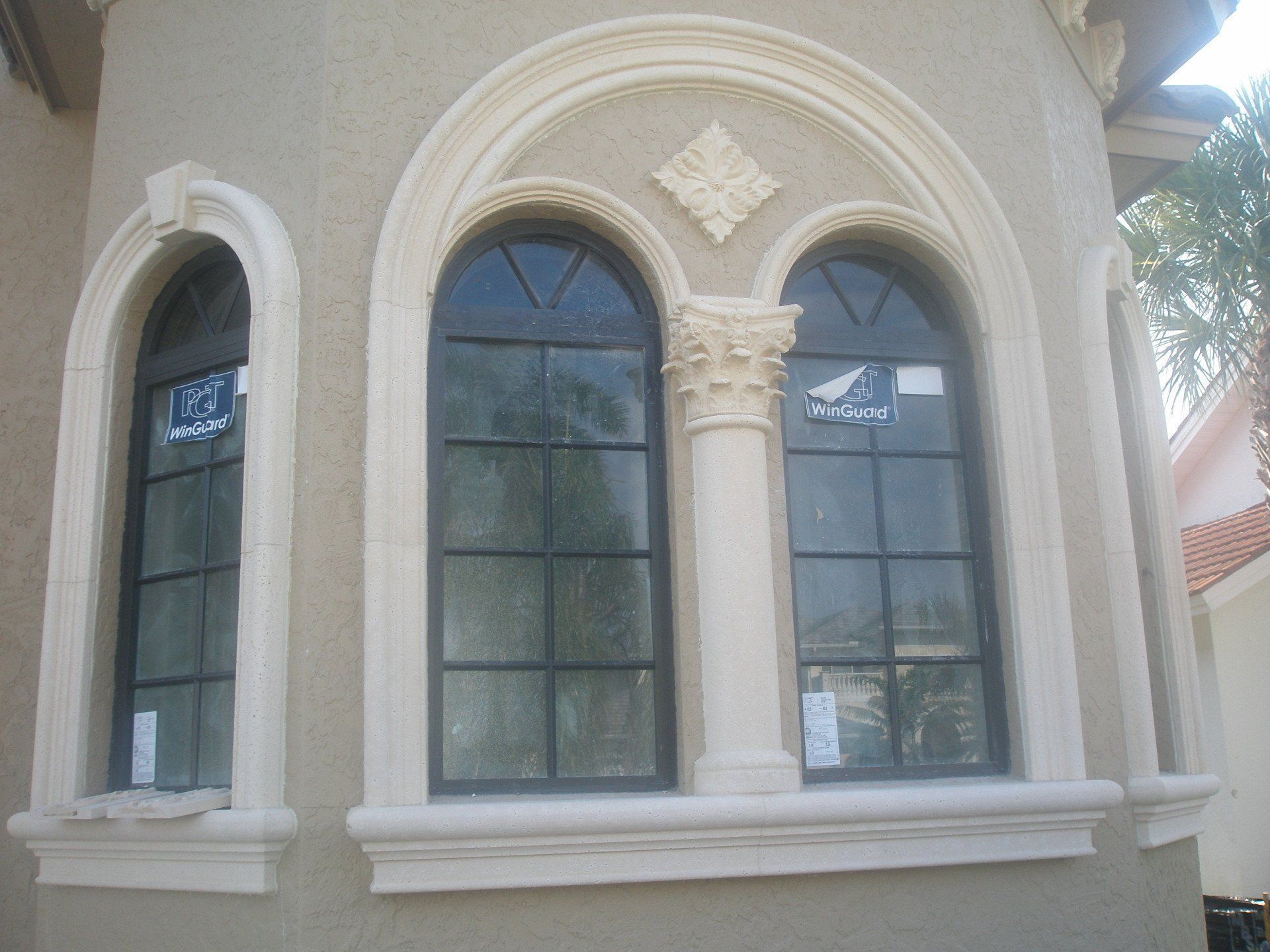 Arched windows on a beige stucco building with decorative trim and a white sill.