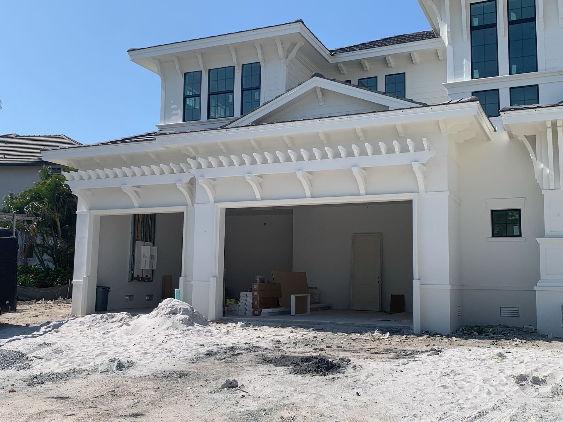 White house under construction with open garage and pergola-like awning, surrounded by construction debris.