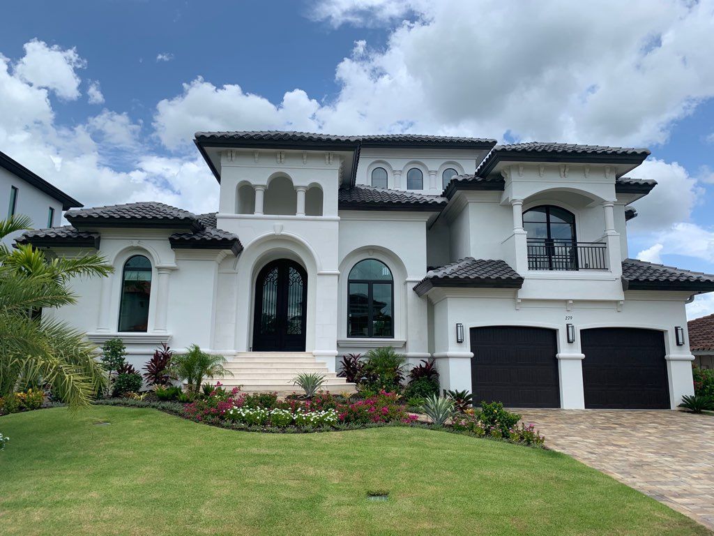 Large white Mediterranean-style house with black roof, arched windows, and a manicured front lawn.