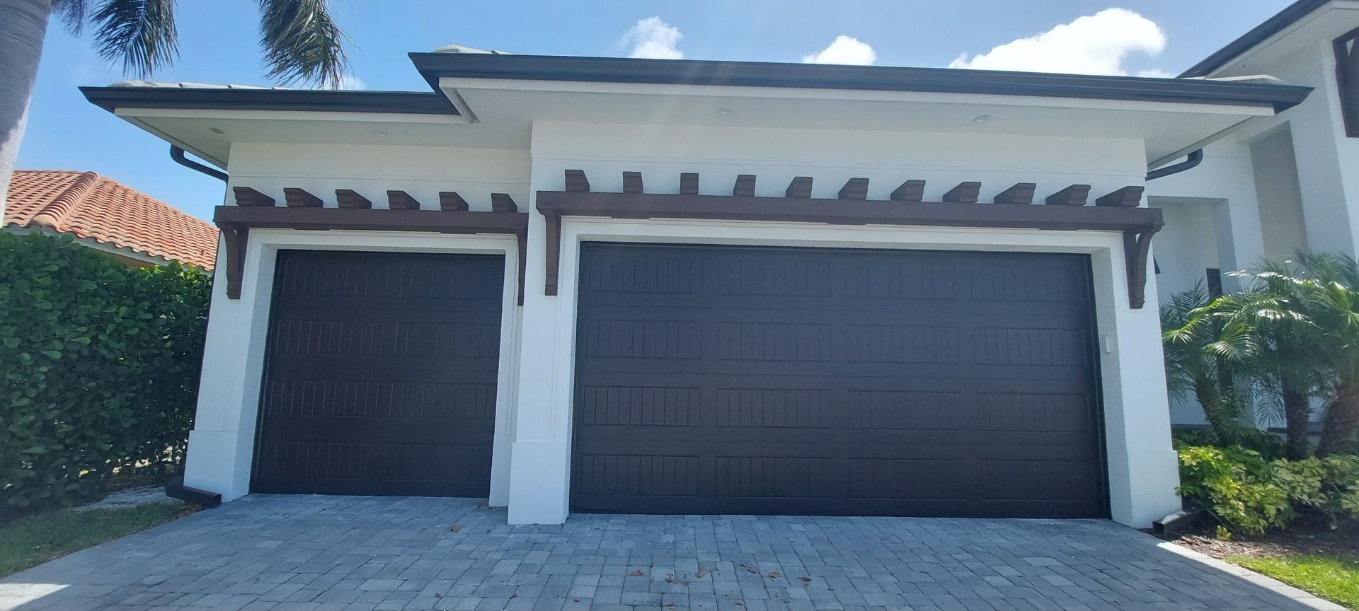Modern two-car garage with white columns, dark doors, and a sloped driveway under a blue sky.