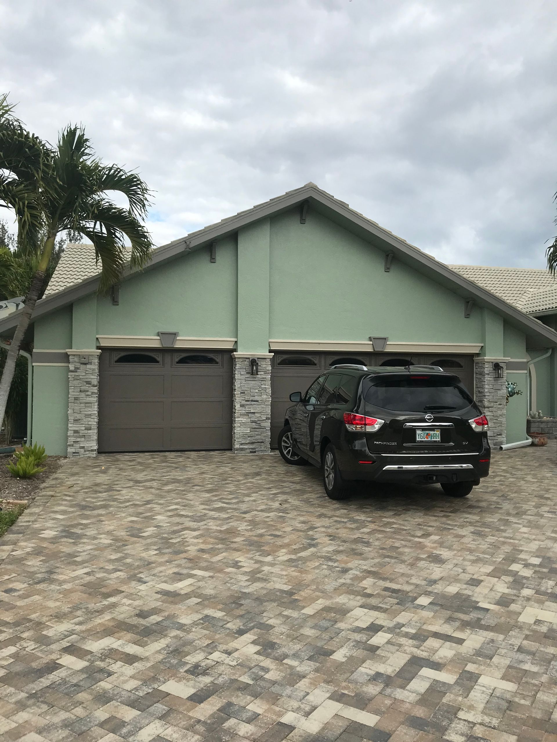 Suburban house with stone facade, two garage doors, and a black SUV parked in the driveway.