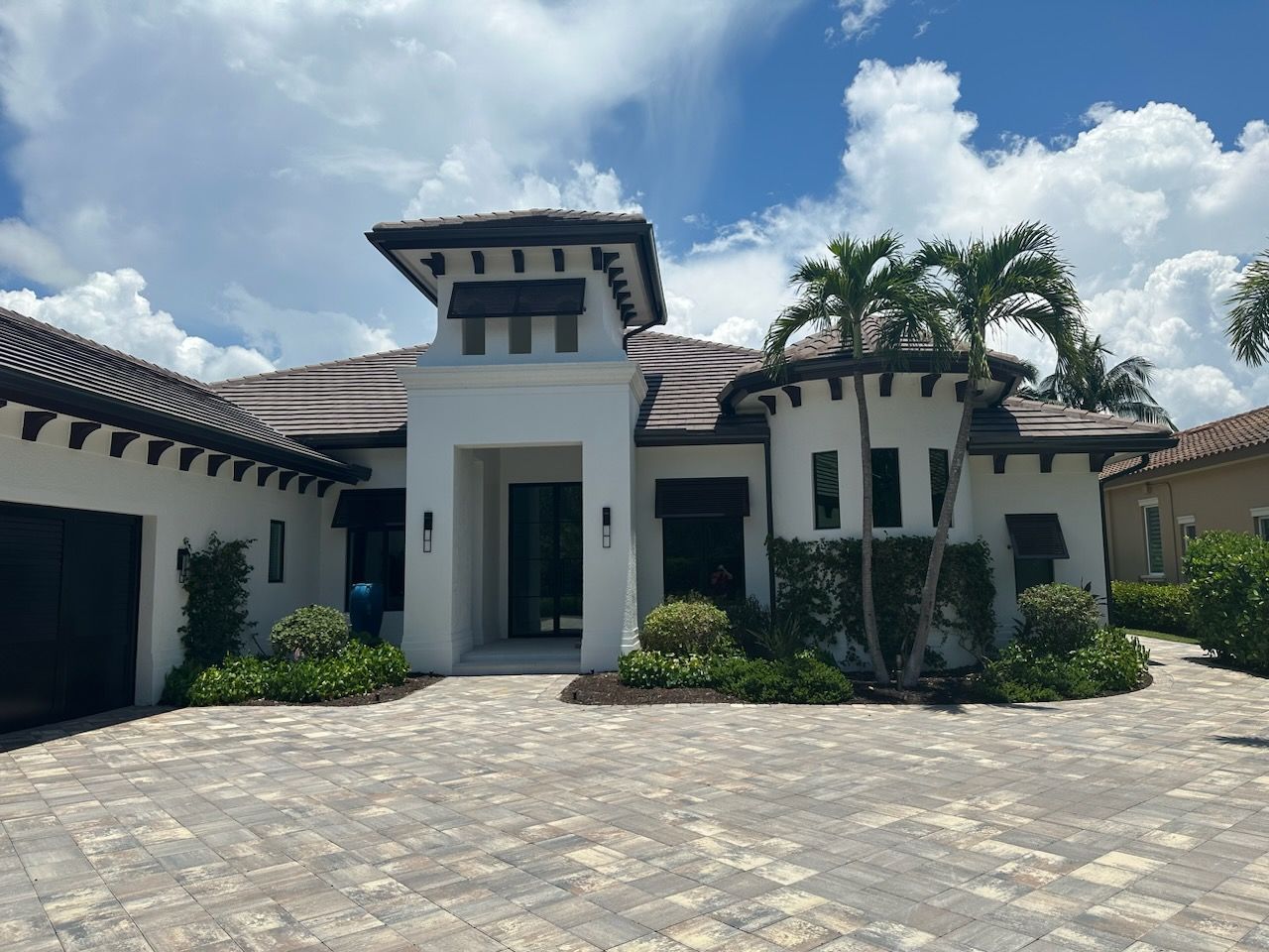 Modern white stucco house with a paved driveway and palm trees under a sunny sky.