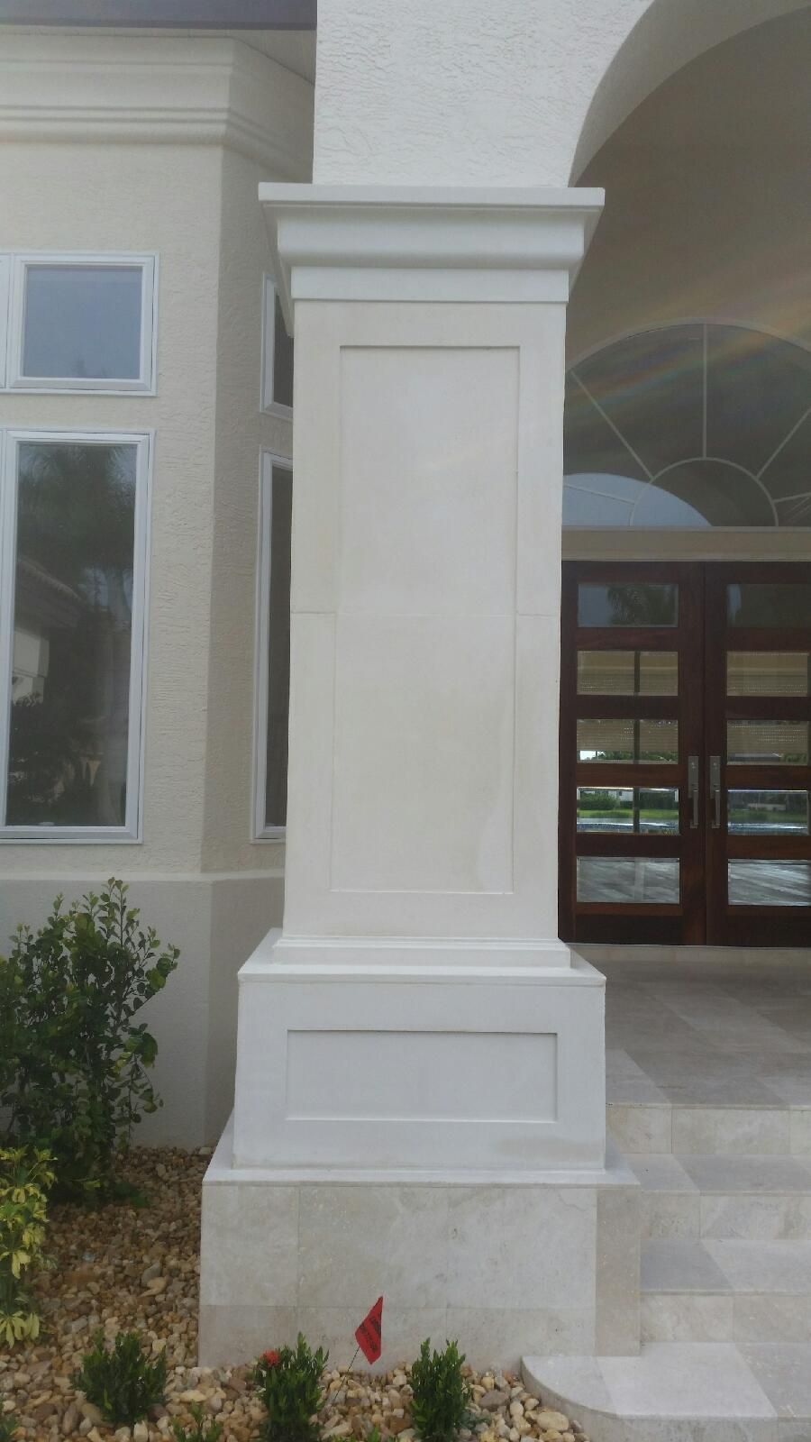 Front entrance of a building with a large beige column and glass doorway under an arched portico.