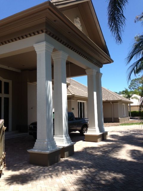 Covered front porch with white columns and a parked black SUV in a sunny residential driveway.
