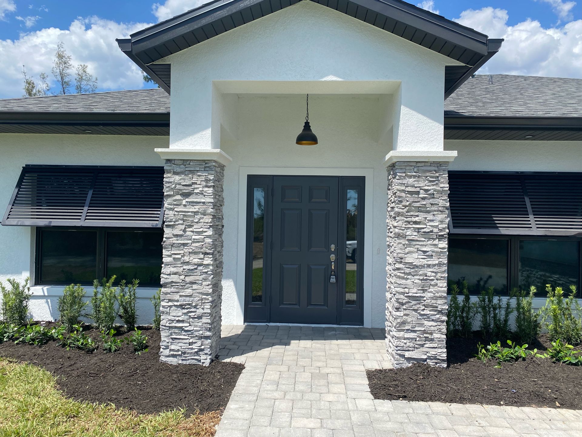 Front entrance of a modern house with stone columns, dark double doors, and a brick walkway.