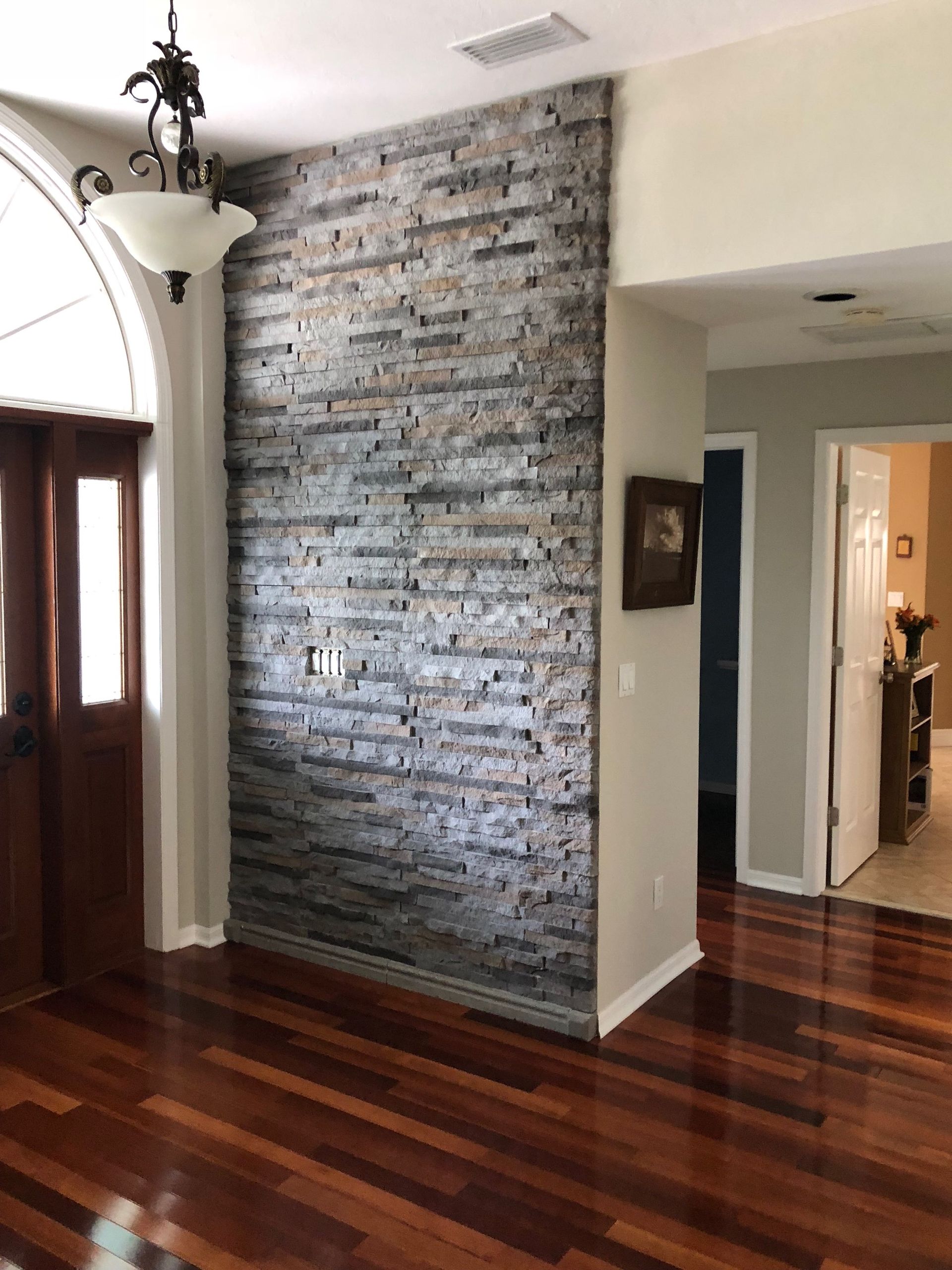 Interior hallway with dark wood floors, a brick accent wall, and a hanging light fixture.