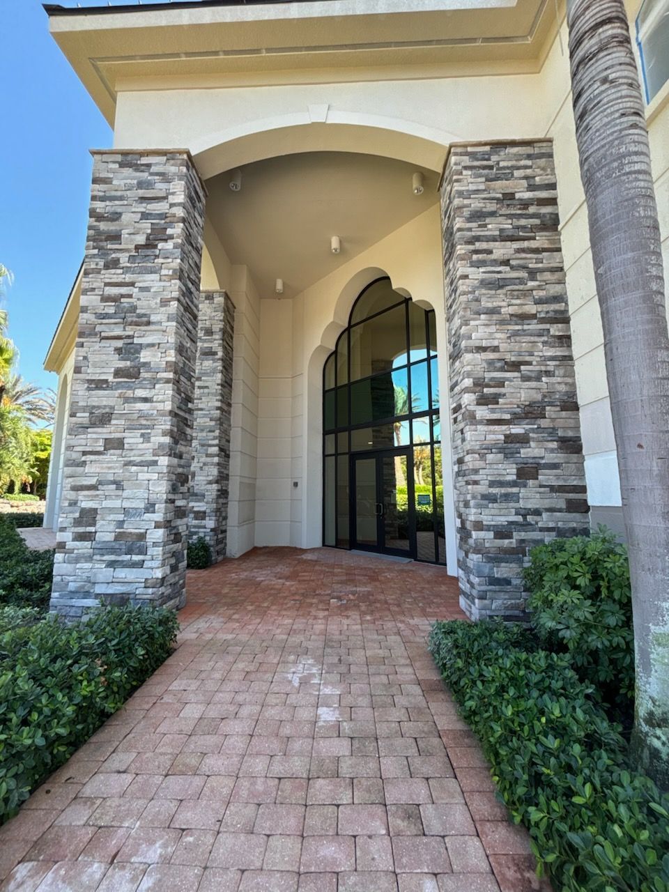 Brick walkway leading to a building entrance with stone columns and a glass doorway