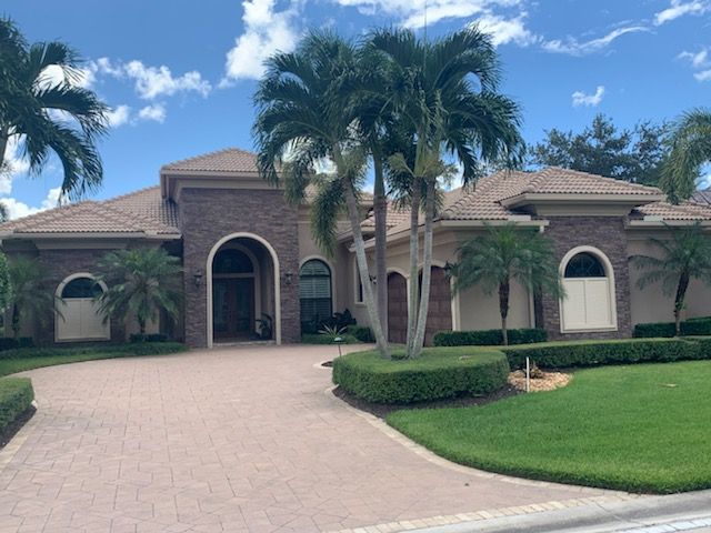 Single-story brick home with palm trees, arched entry, and curved driveway under a blue sky.