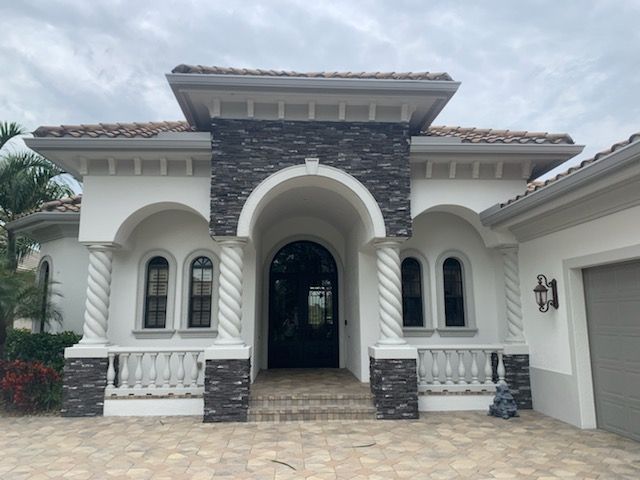 Mediterranean-style house exterior with arched entry, stone facade, and white stucco trim.