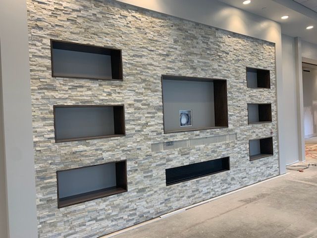 Stone wall with built-in rectangular niches in a modern lobby hallway.