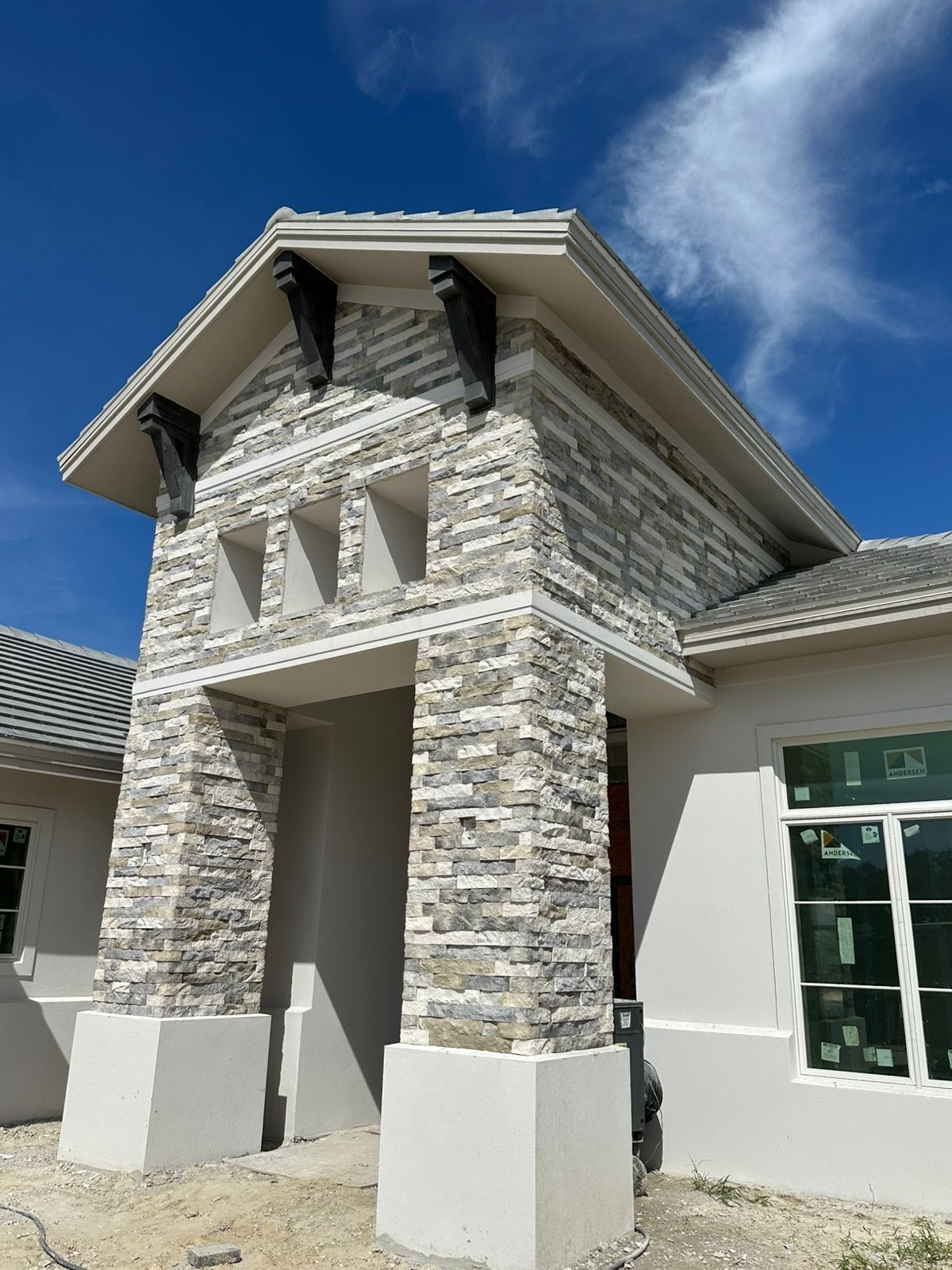 Stone-clad building entrance with tall columns and a gabled roof under a blue sky.