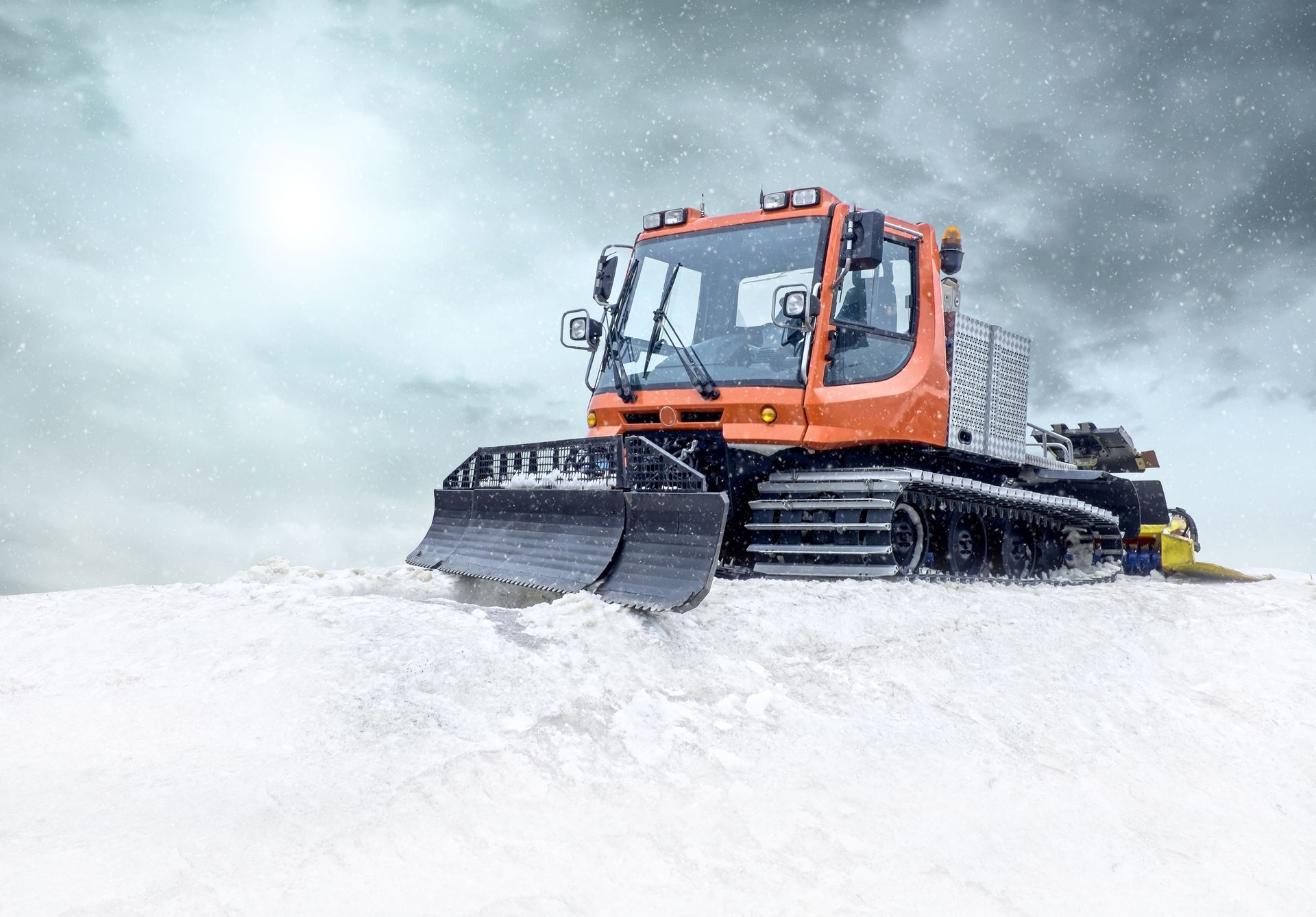 Orange snow groomer plowing fresh snow on a cloudy, snowy day.