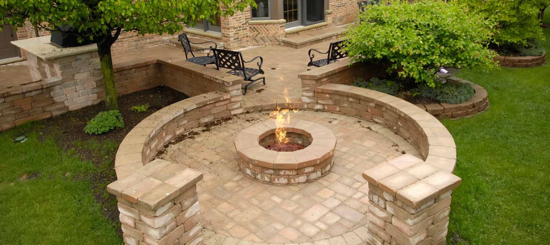 Outdoor patio with fire pit, surrounded by brick seating and greenery.