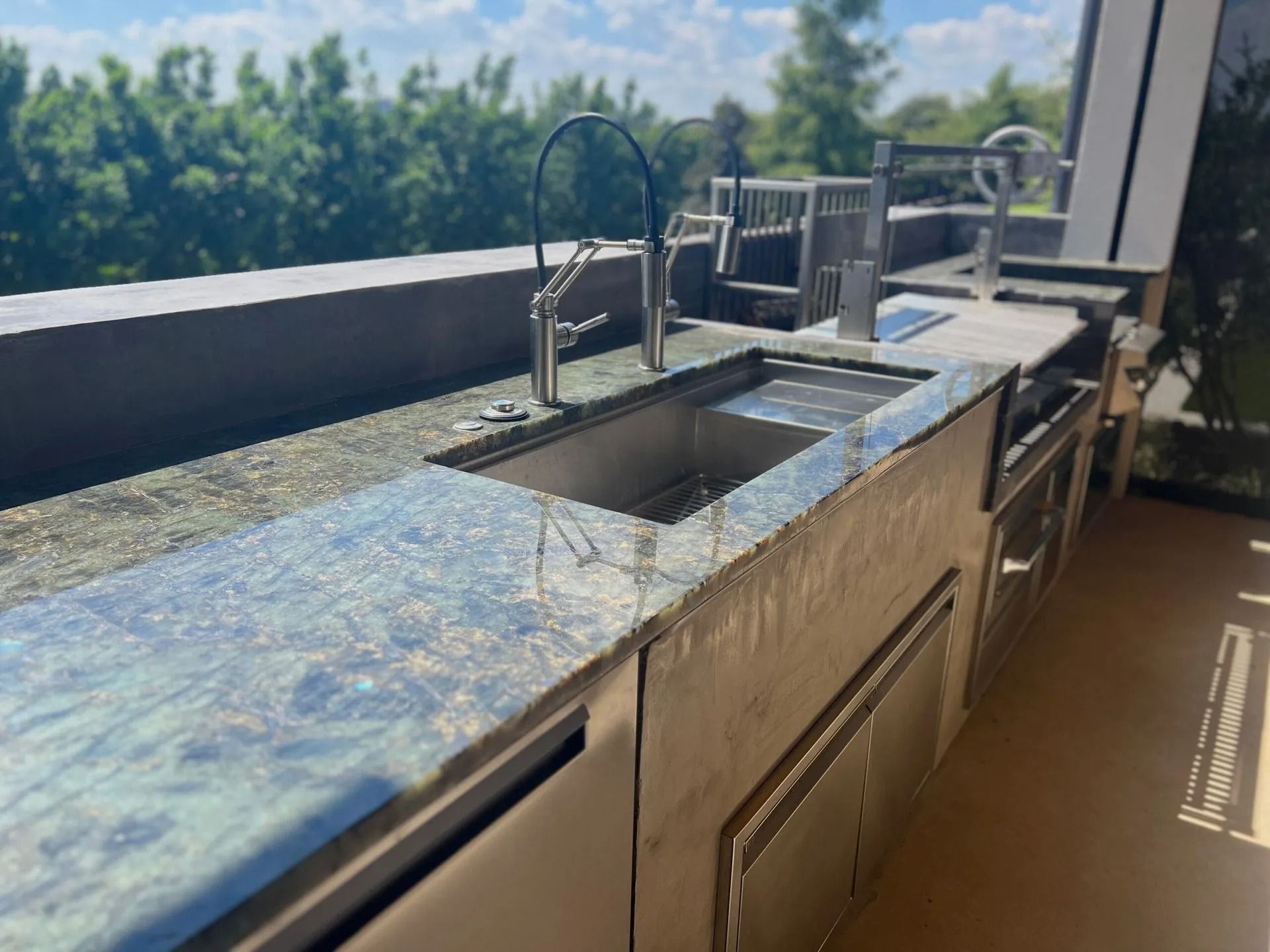 Outdoor granite countertop with a built-in sink and faucet on a balcony, with trees in the background
