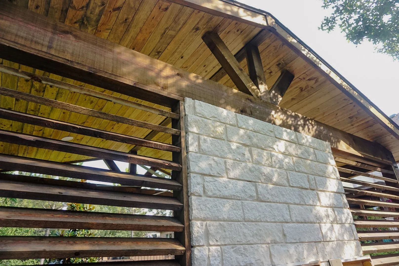 Weathered wooden shed with a corrugated metal roof and a cinder block wall in sunlight