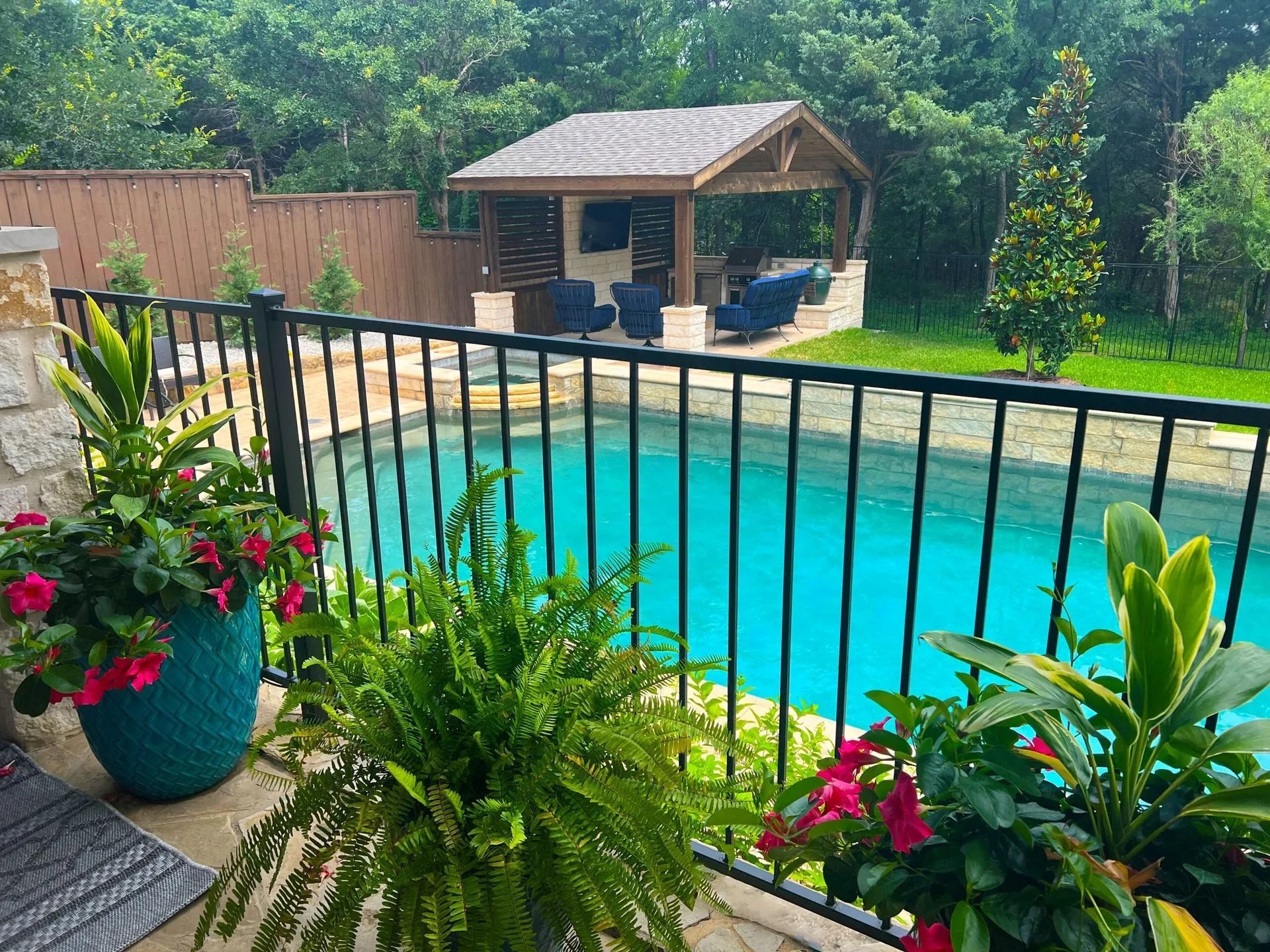 Backyard pool with black fence, gazebo, tropical plants, and bright blue water