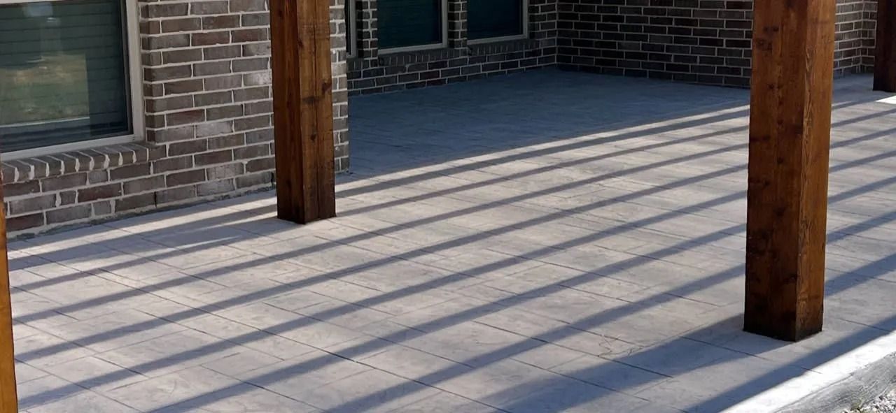 Wooden porch with brick wall and shadowed railings, showing sunlight on the concrete floor.