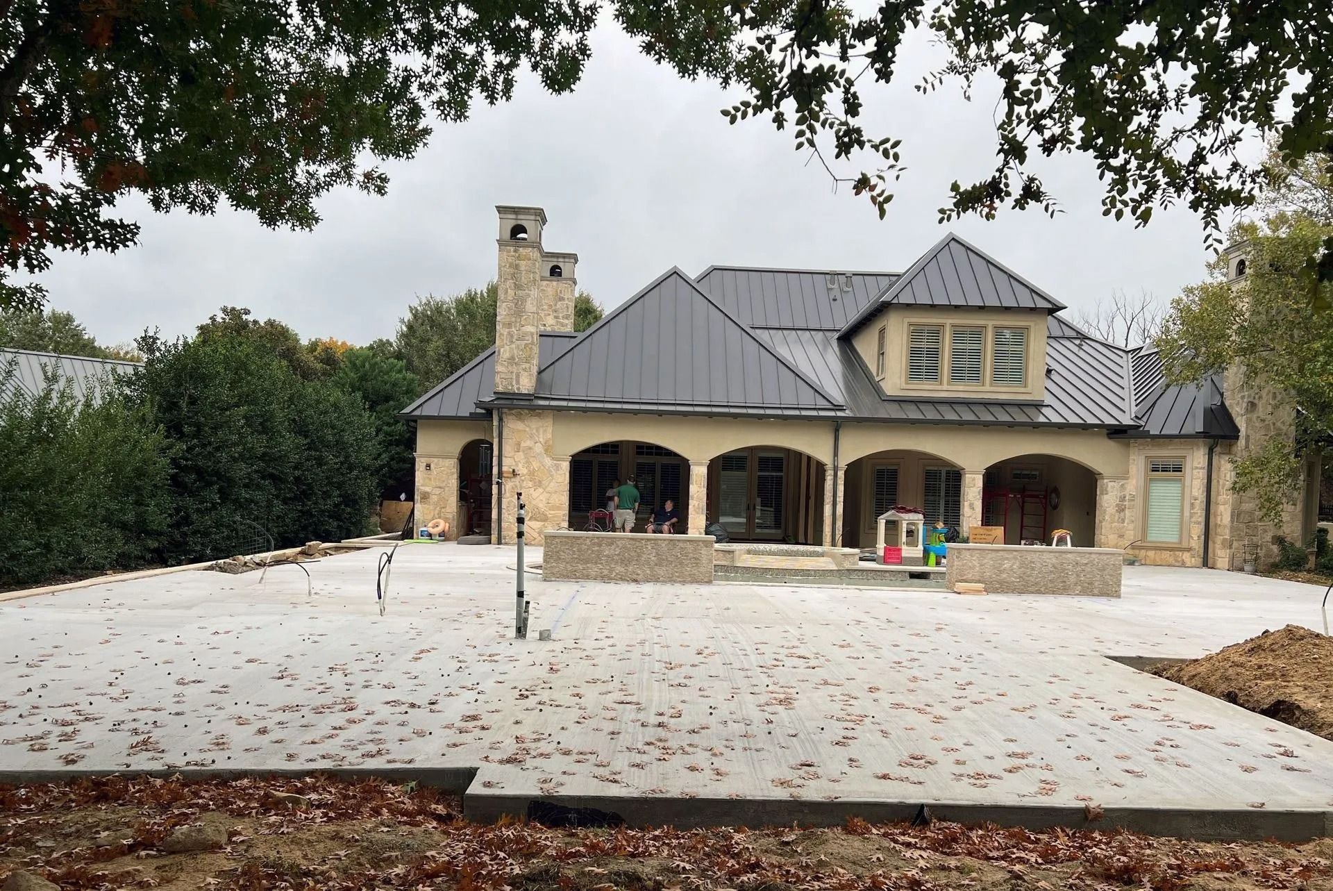 Large stone house with a dark roof, arched porch, and broad driveway under overhanging trees