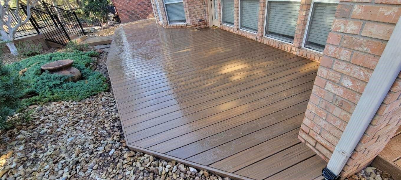 Wet wooden deck beside a brick house with sliding glass doors and garden beds on the left.