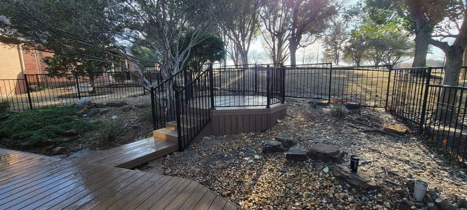 Burned wooded park area with blackened ground, trees, and a metal fence in sunlight