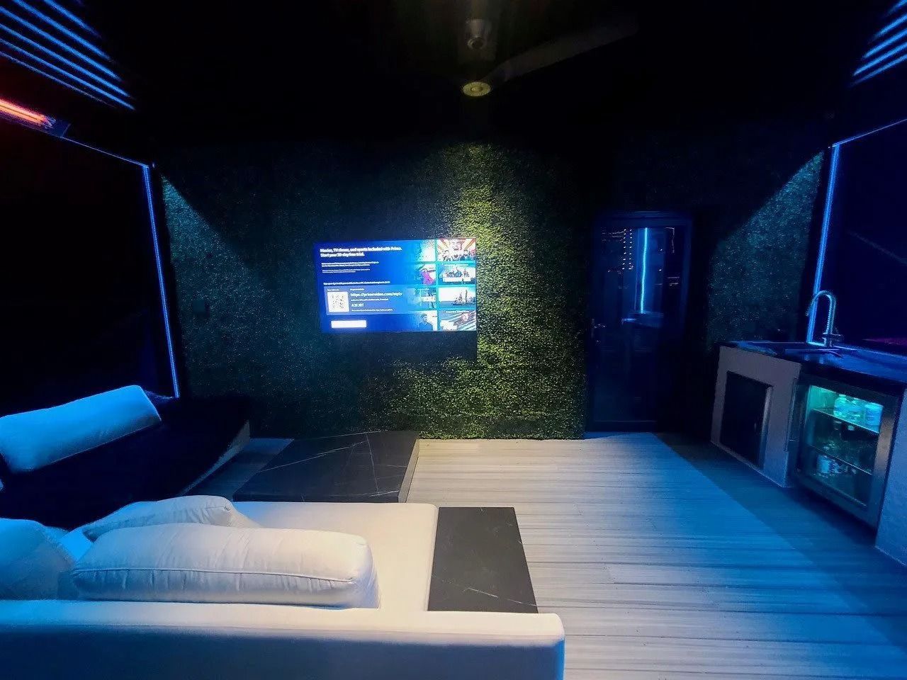 Modern bedroom with blue LED lighting, wall-mounted TV, and a bed beside a glass-walled bathroom