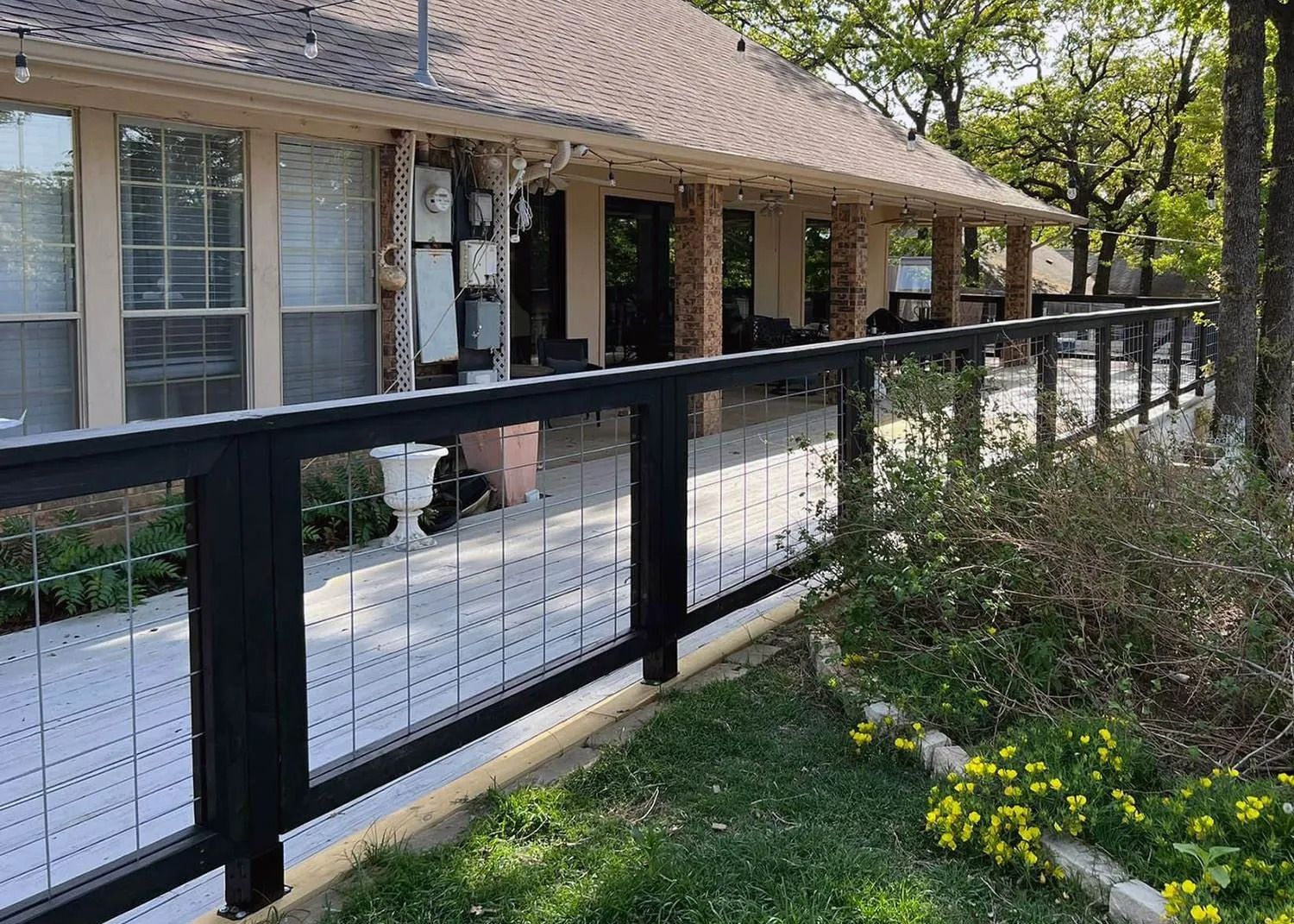 Black metal fence along a brick house with a porch and landscaped front yard.