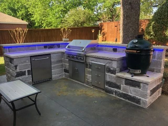 Outdoor backyard kitchen with built-in grill, smoker, sink, and blue-lit countertop seating area.