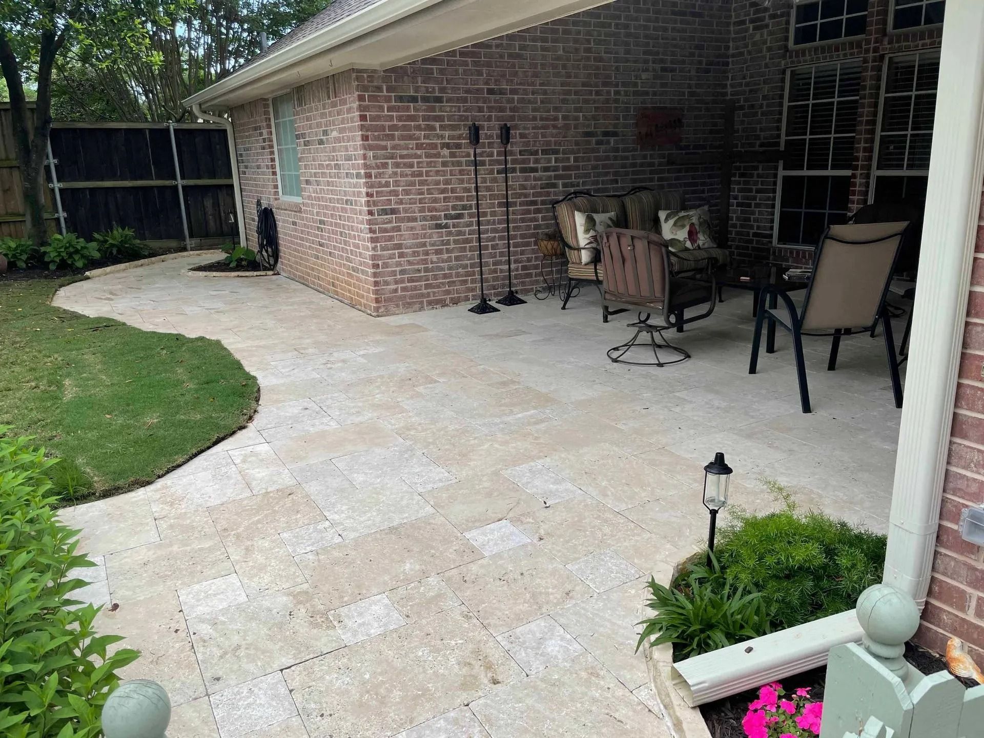 Brick patio with stone pavers, outdoor dining chairs, and a curved walkway beside a house.