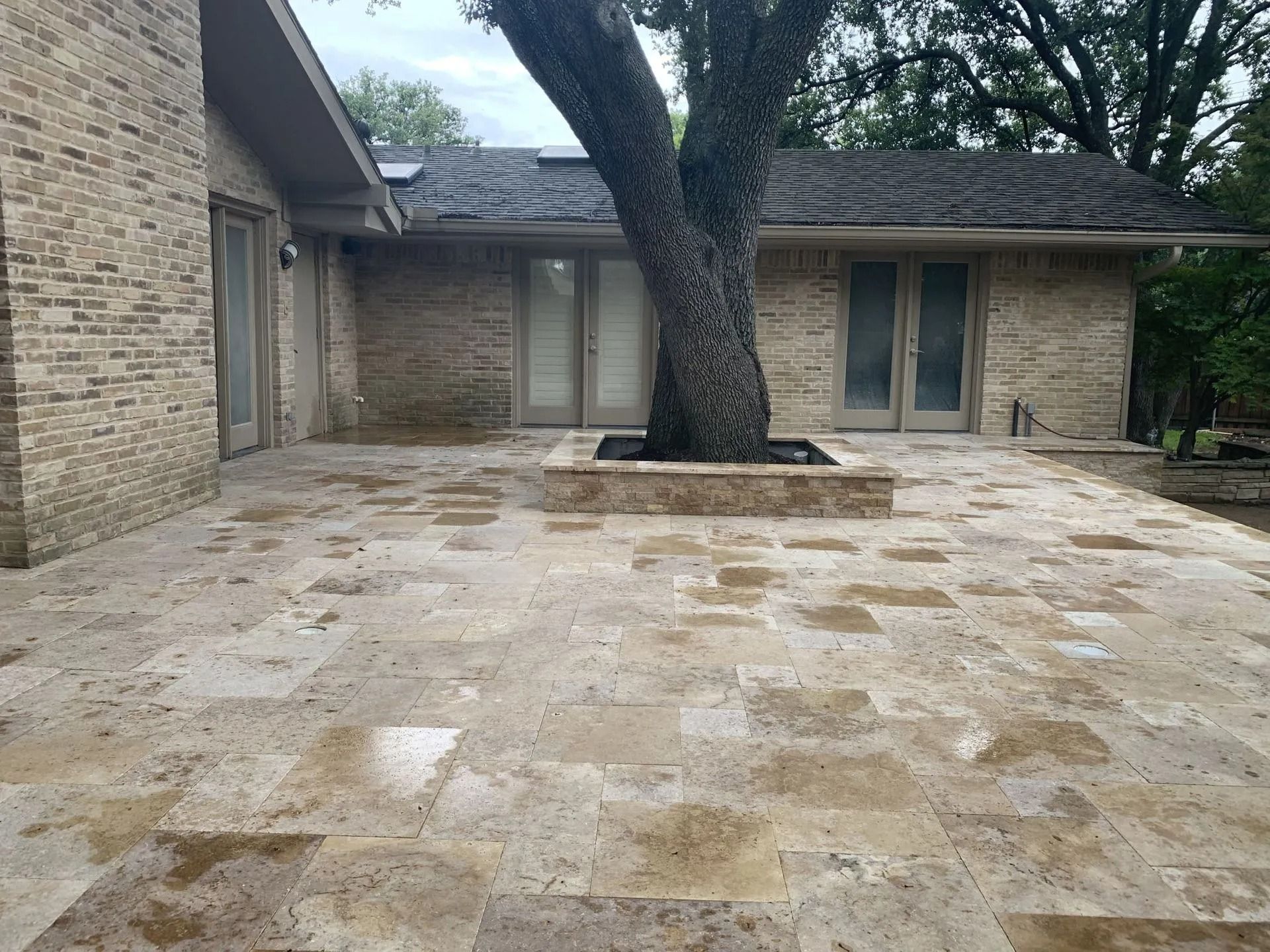 Stone patio courtyard with a large tree beside a brick house and sliding glass doors