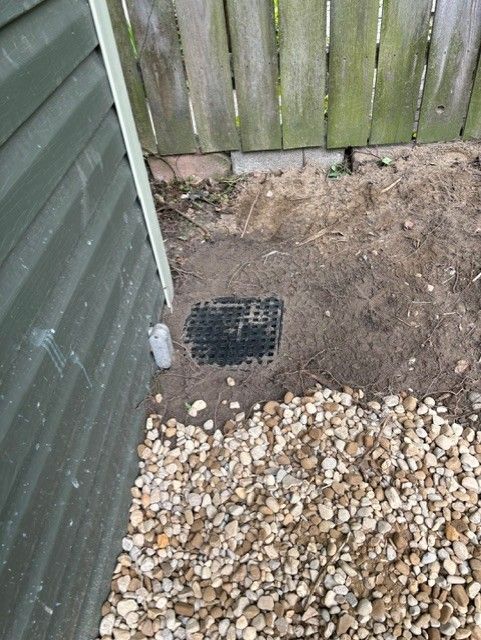 A drain in the ground next to a wooden fence