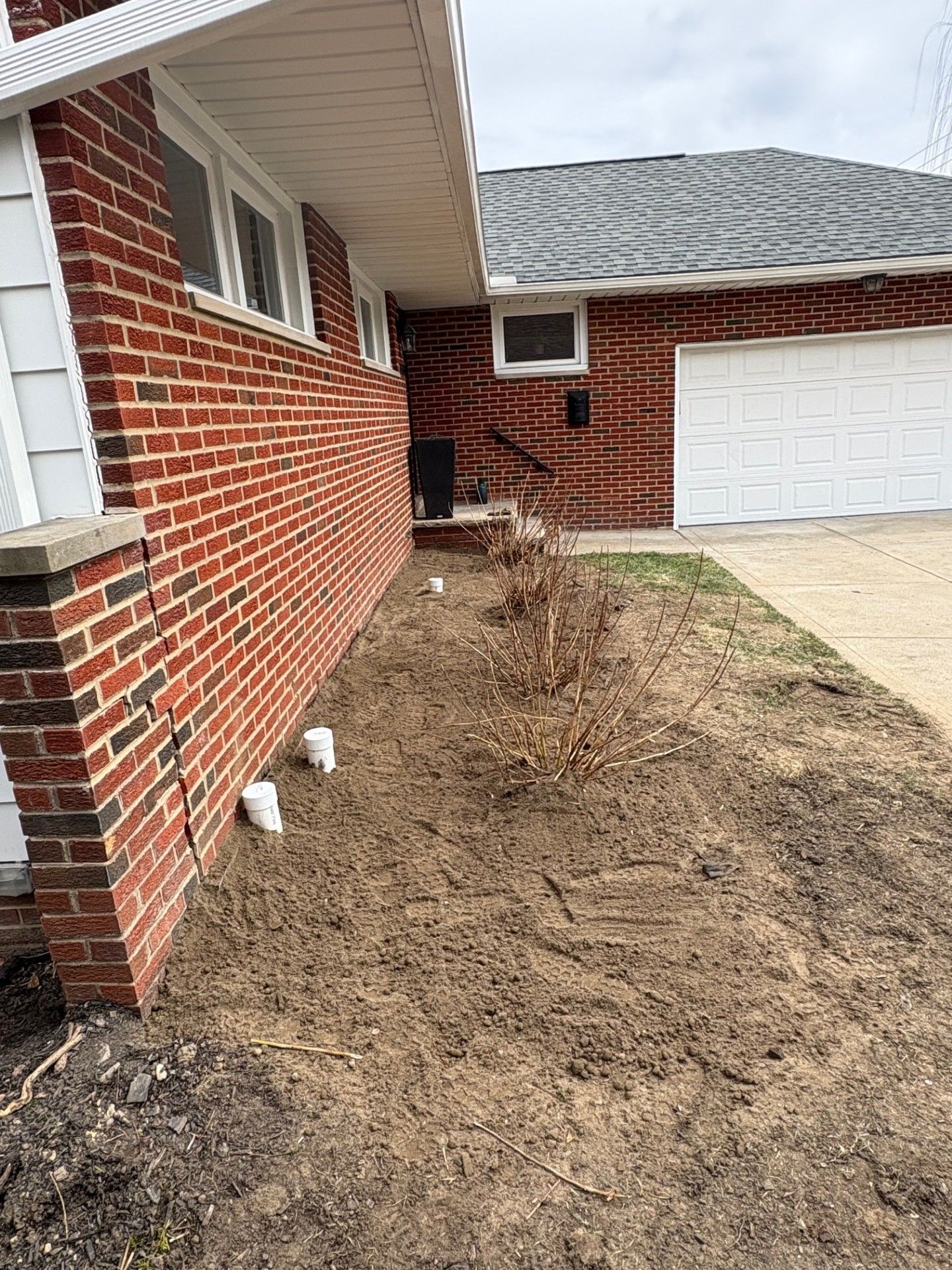 A brick house with a white garage door and a dirt yard in front of it.