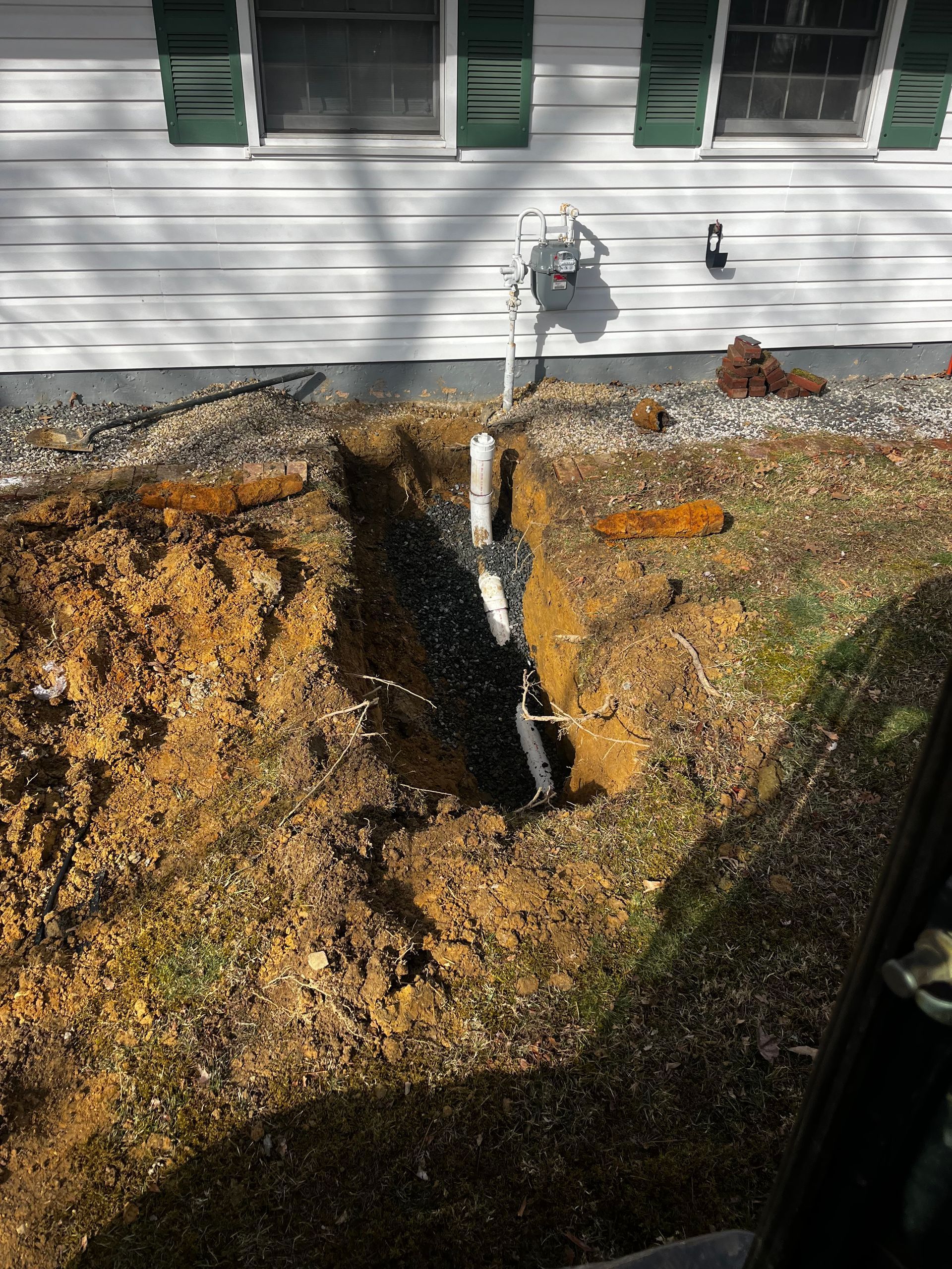 A pipe is being installed in a hole in the ground in front of a house.