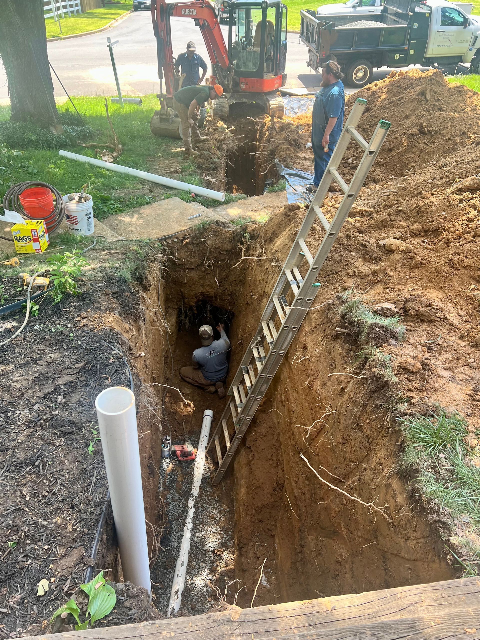 A man is sitting in a hole in the ground with a ladder.