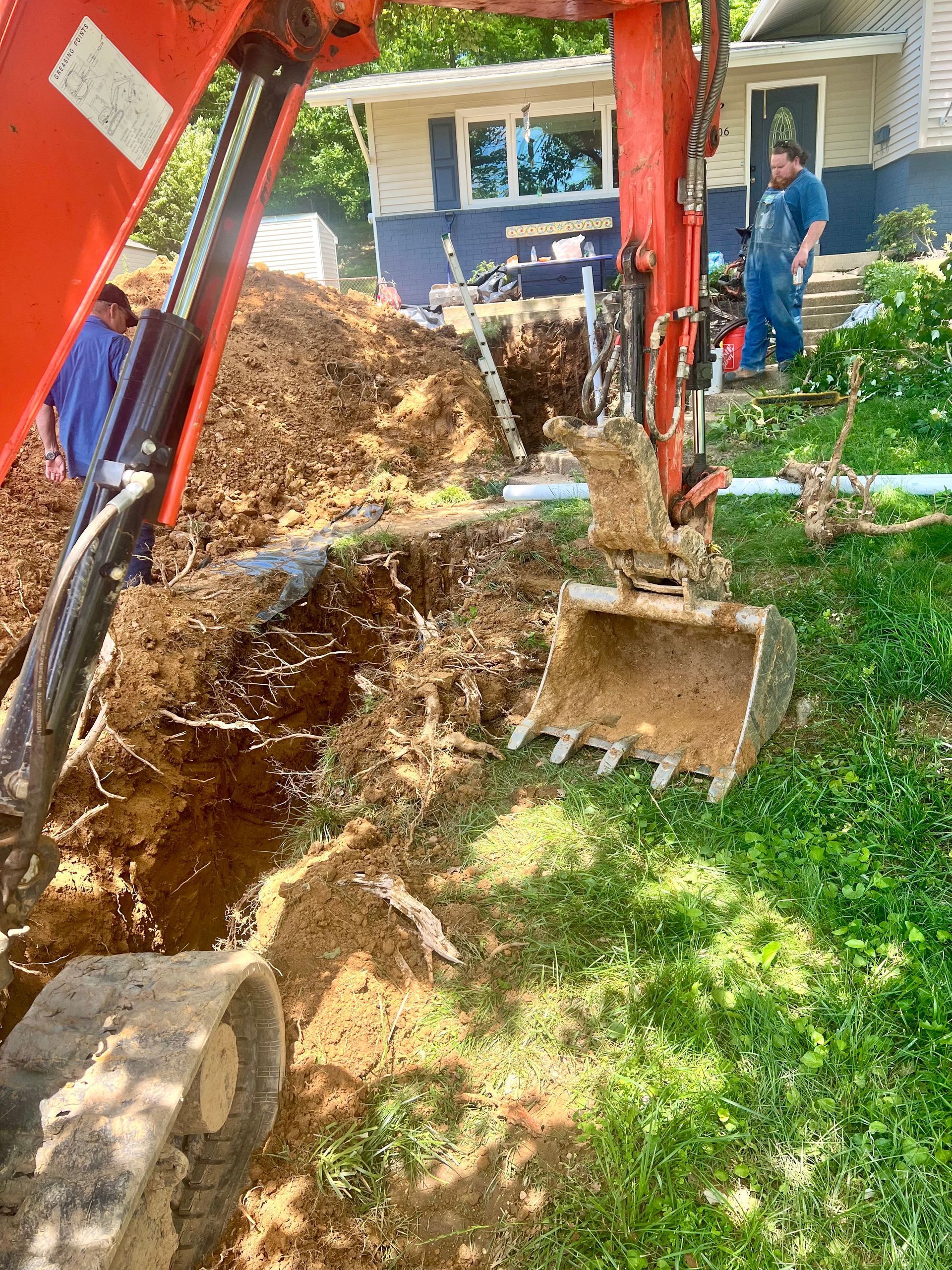 An excavator is digging a hole in the ground in front of a house.