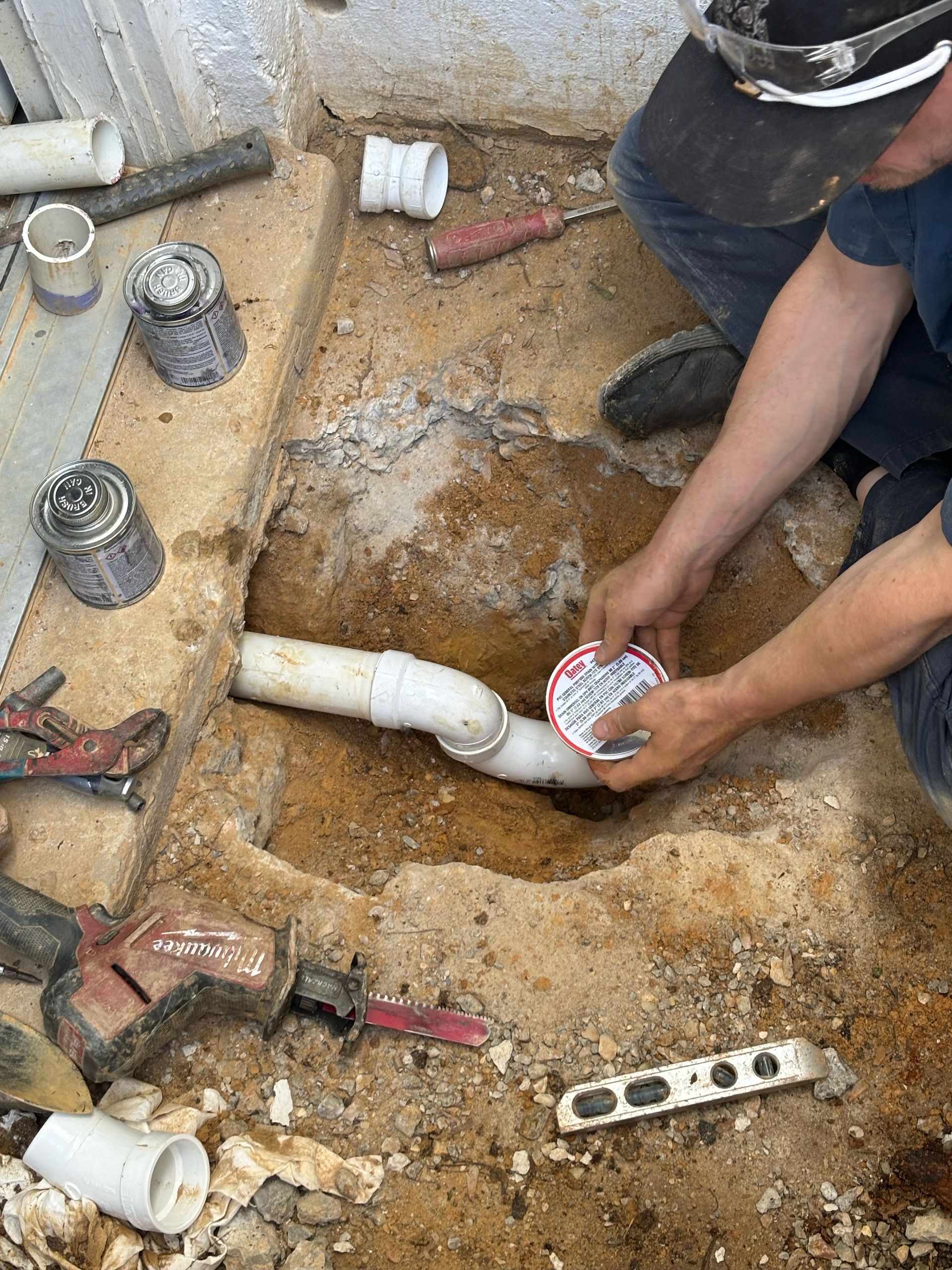 A man is kneeling down in the dirt fixing a pipe.