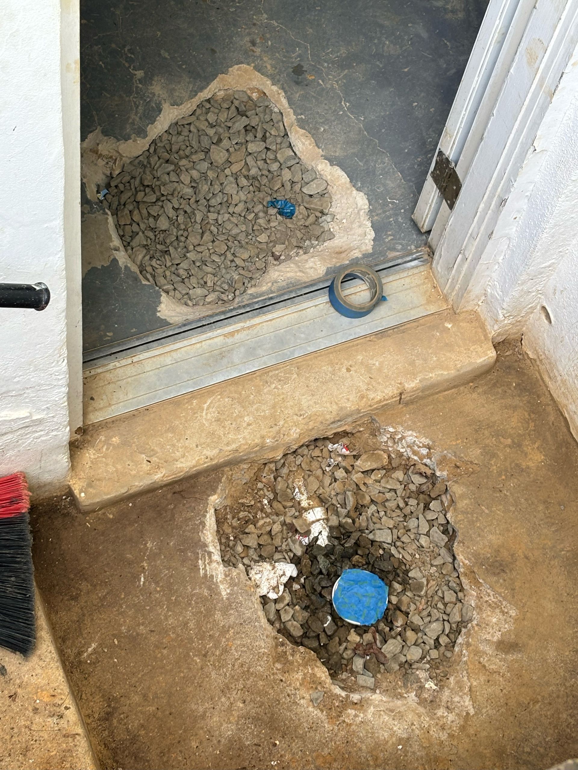 A hole in the ground next to a door with a blue pipe in it.