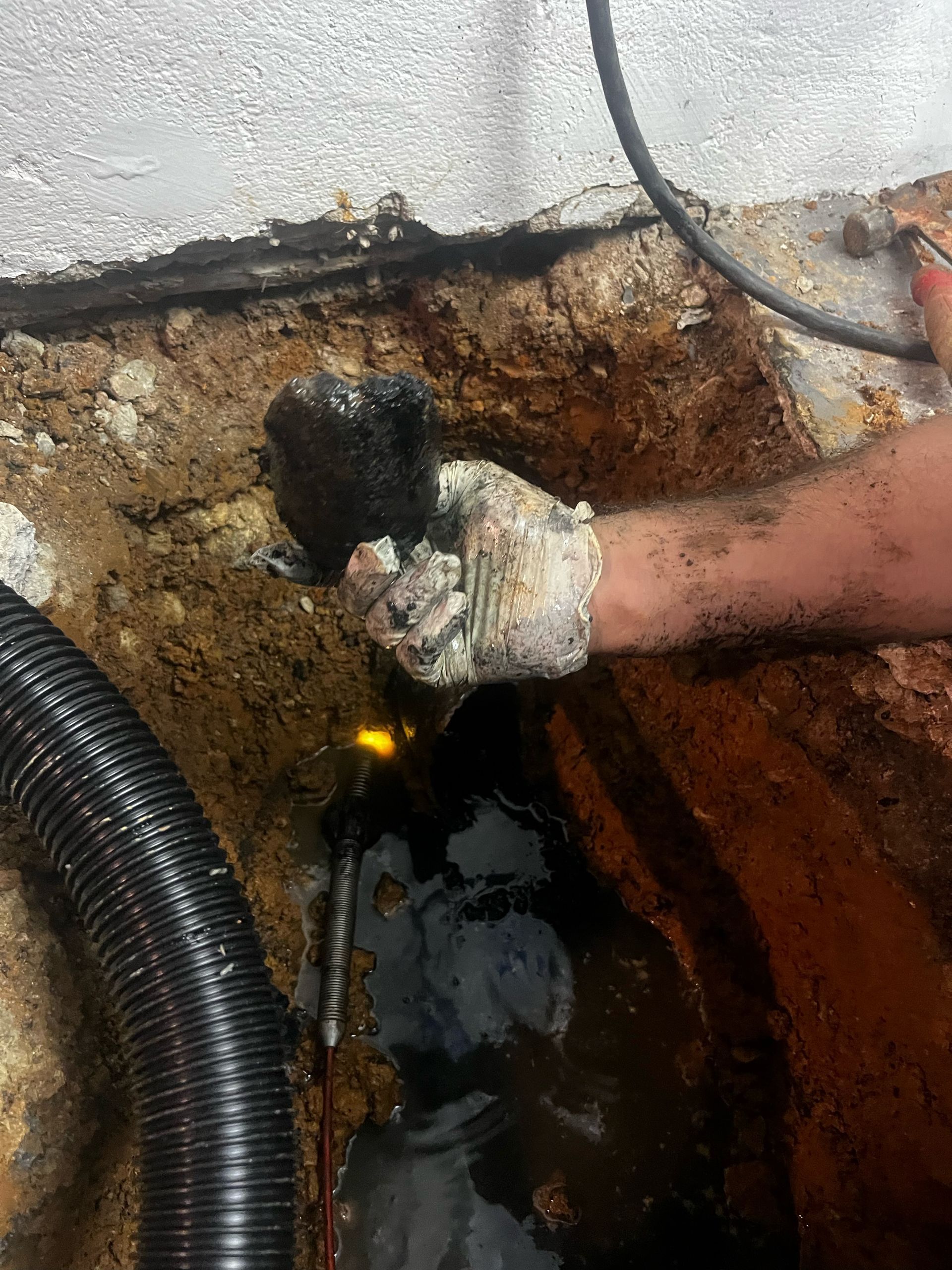 A person is holding a hose in a hole in the ground.