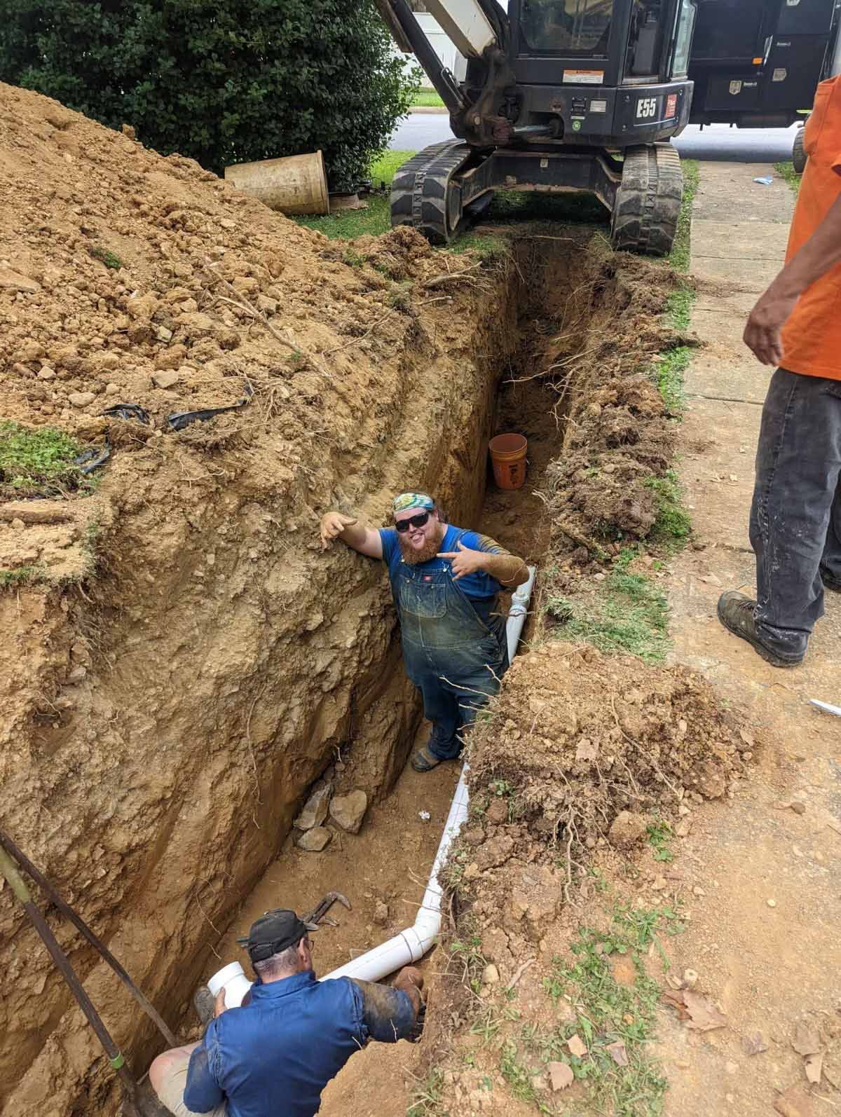 A man is standing in a trench next to a bulldozer.