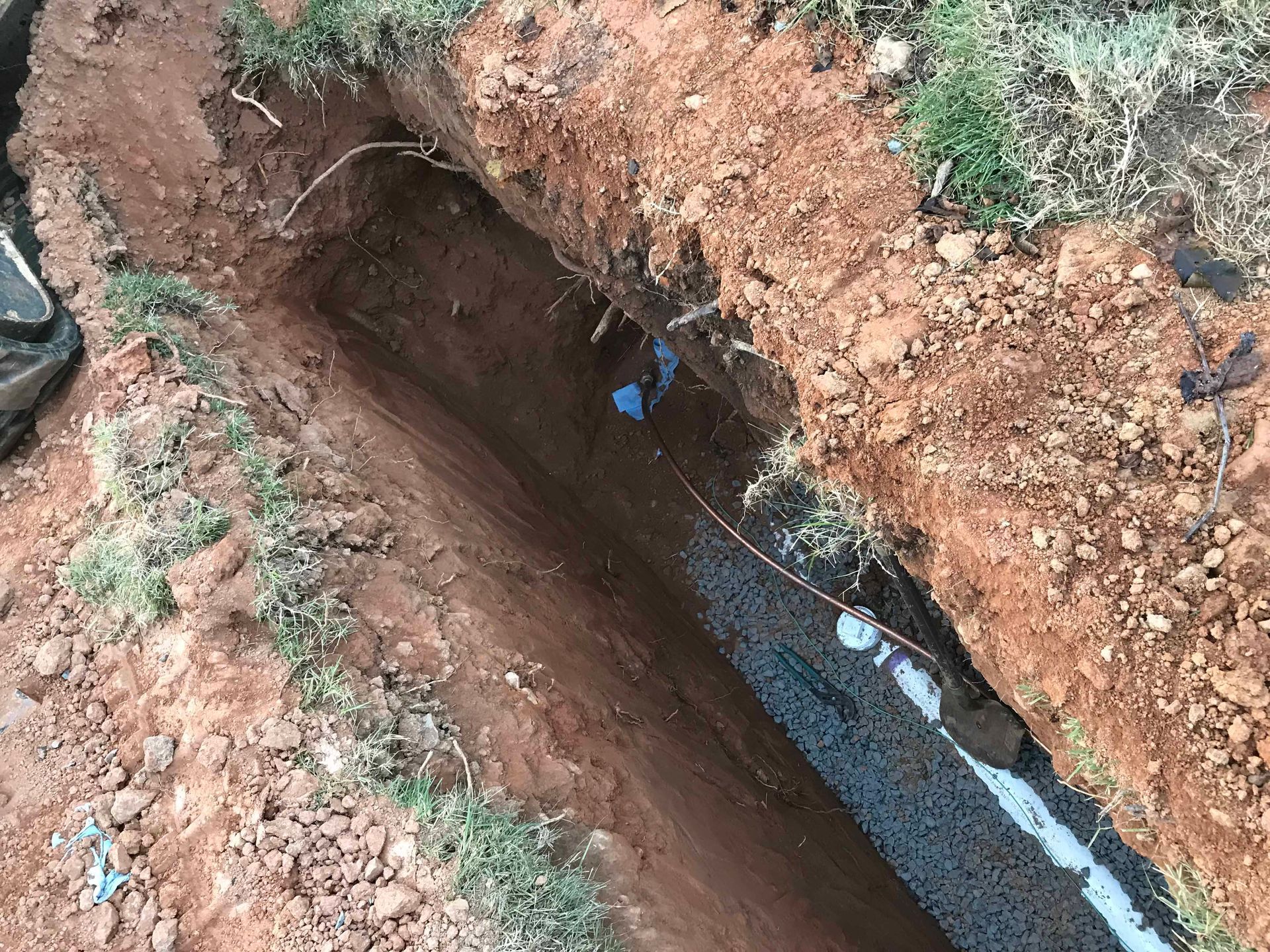 A person is digging a hole in the ground next to a pipe.