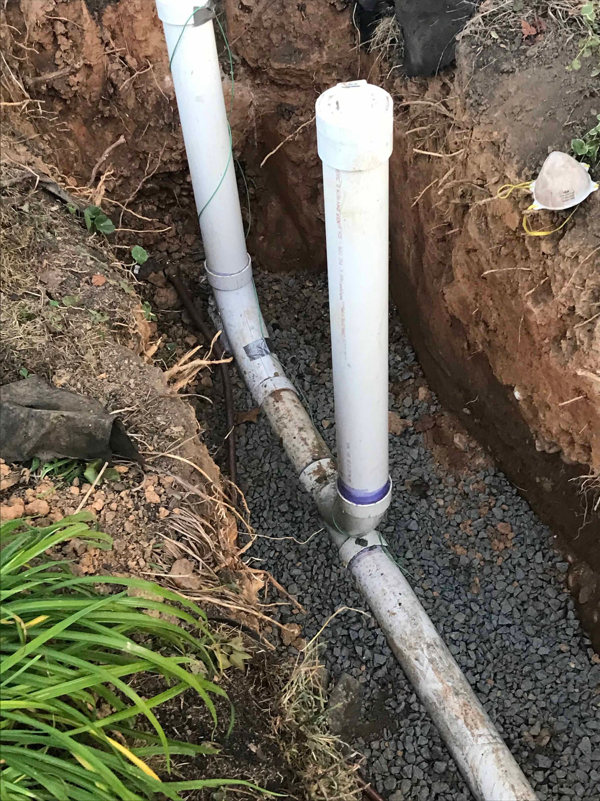Two white pipes are connected to each other in a hole in the ground.